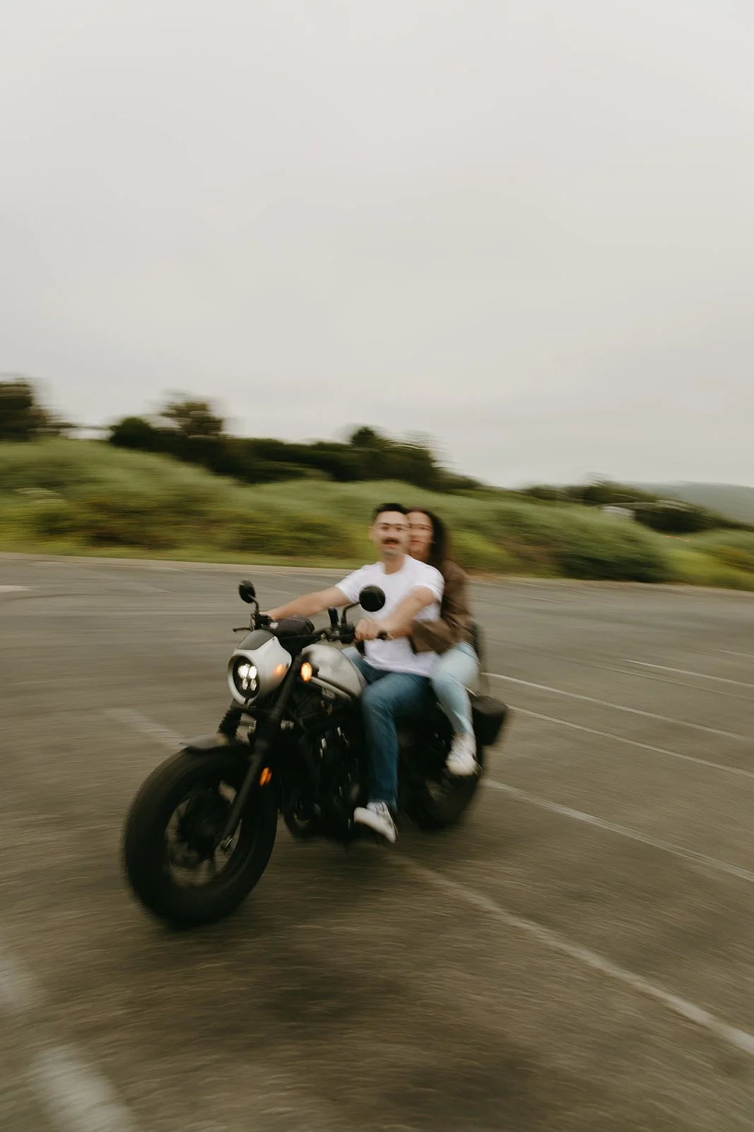 A slightly blurred motion shot of a couple riding a motorcycle through an open lot, surrounded by greenery — capturing the adventurous side of romantic engagement photo ideas.