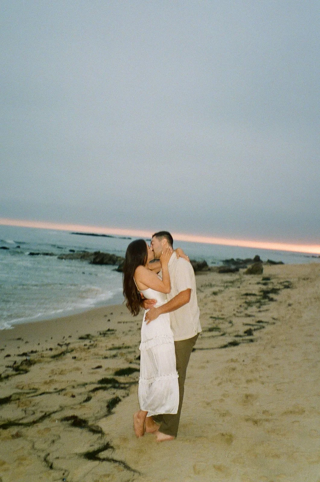A slightly blurred image of the couple kissing at the shoreline, framed by soft lighting and a peaceful sky.