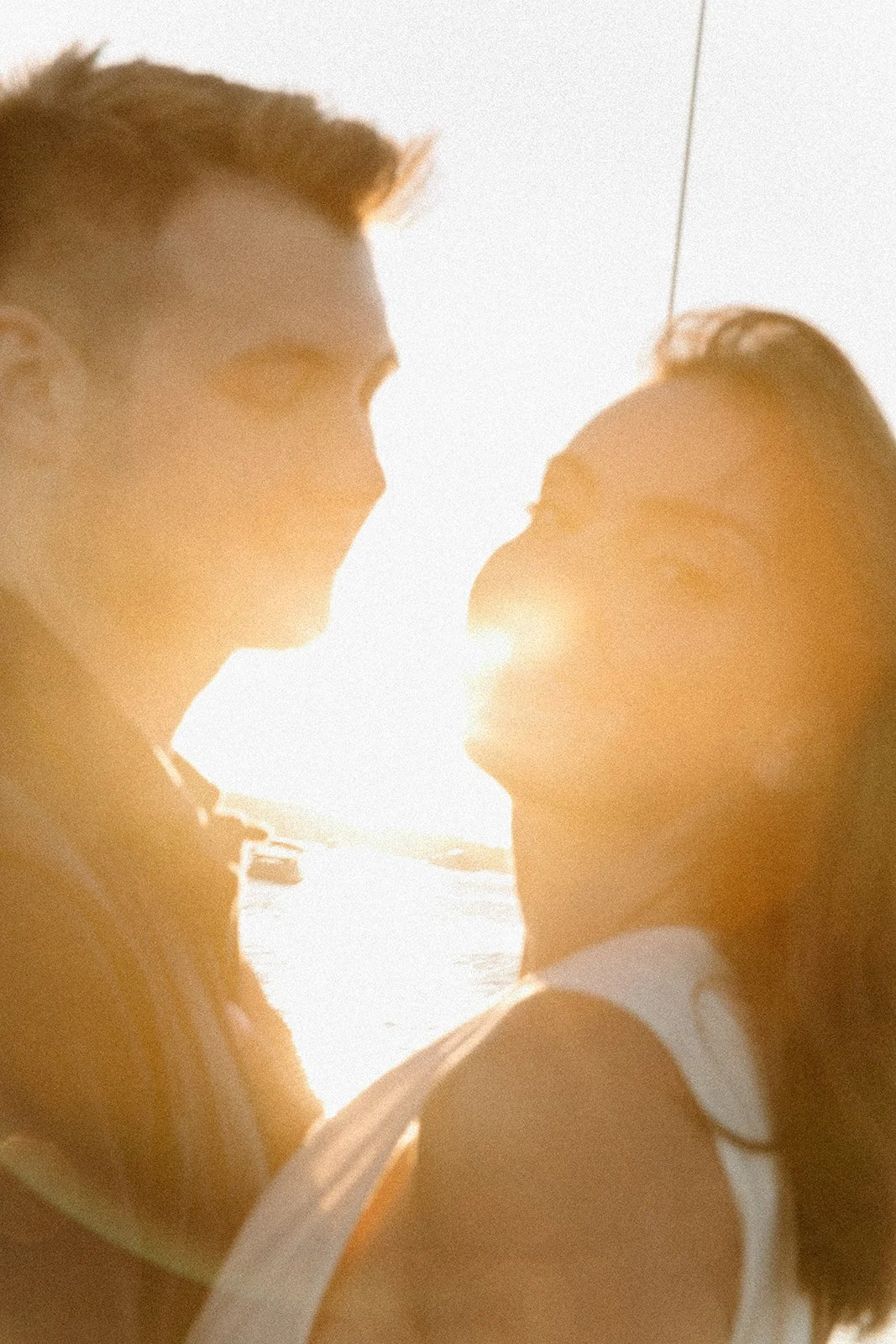 Blurry sunflare photo of a couple, the girl is looking towards the camera while the man is lovingly looking at her.