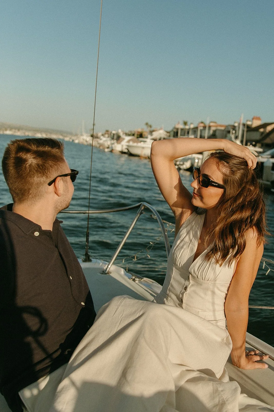 Couple relaxing on a sailboat while enjoying the view, sailboat engagement photos with a peaceful marina in the background.
