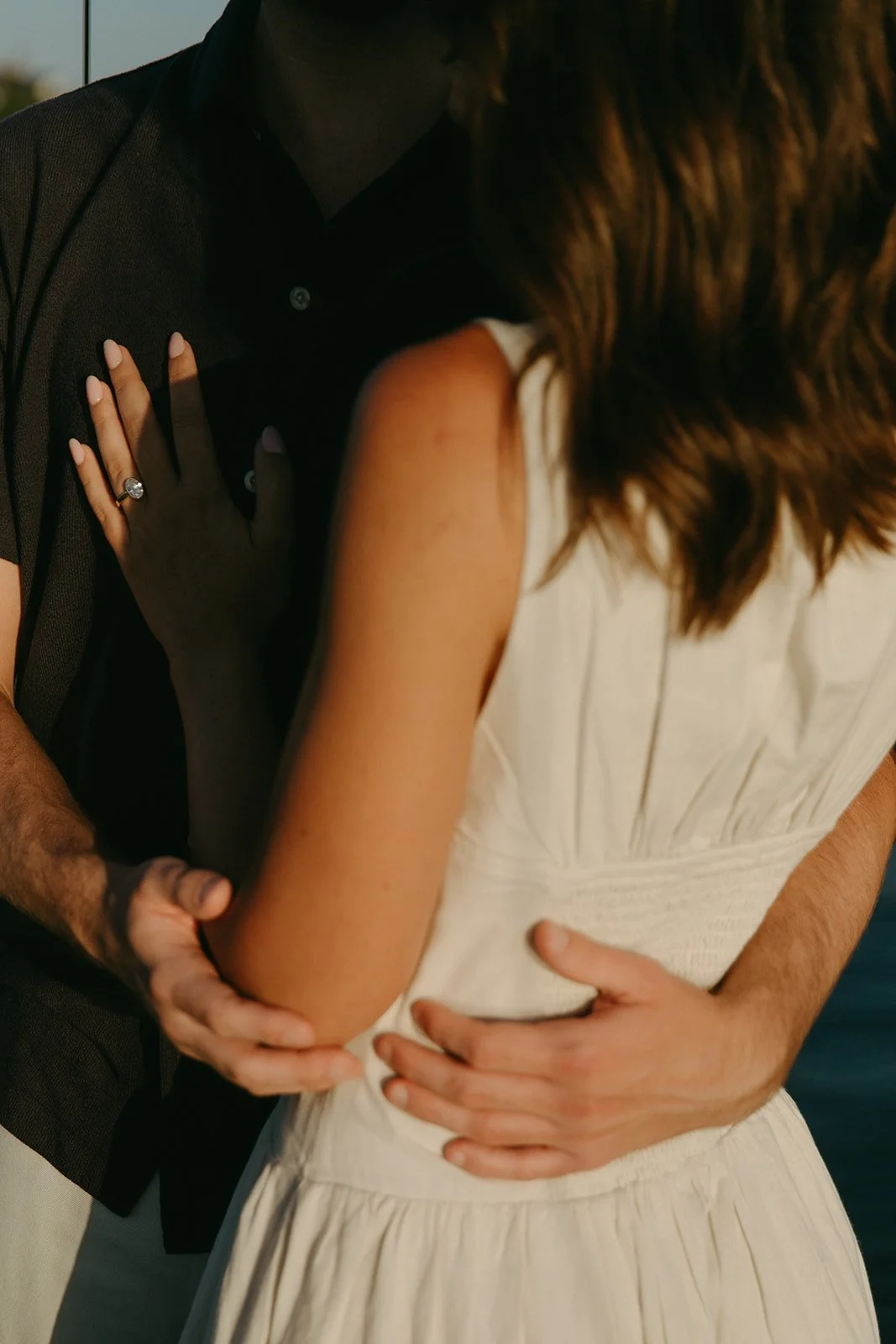 Close-up of the woman’s hand with an engagement ring resting on her partner's chest, sunset sailboat engagement photos capturing romantic details.