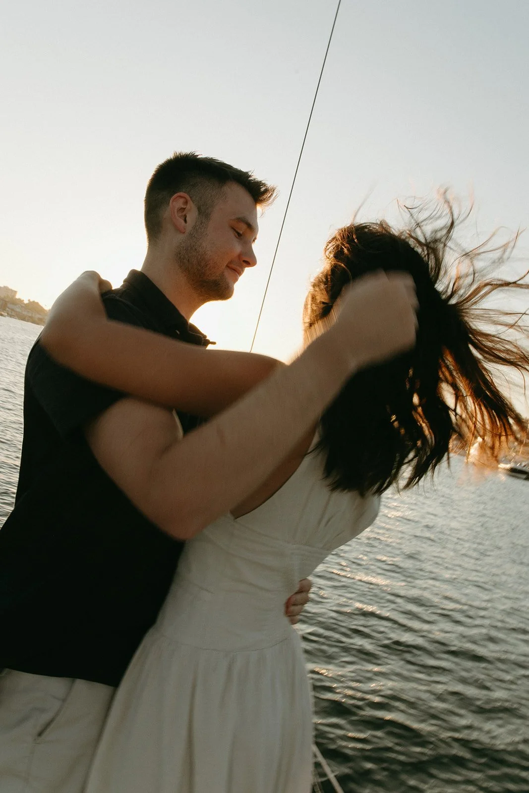 Couple sharing a soft moment as the wind blows her hair on a boat, sailboat engagement photos during golden hour.