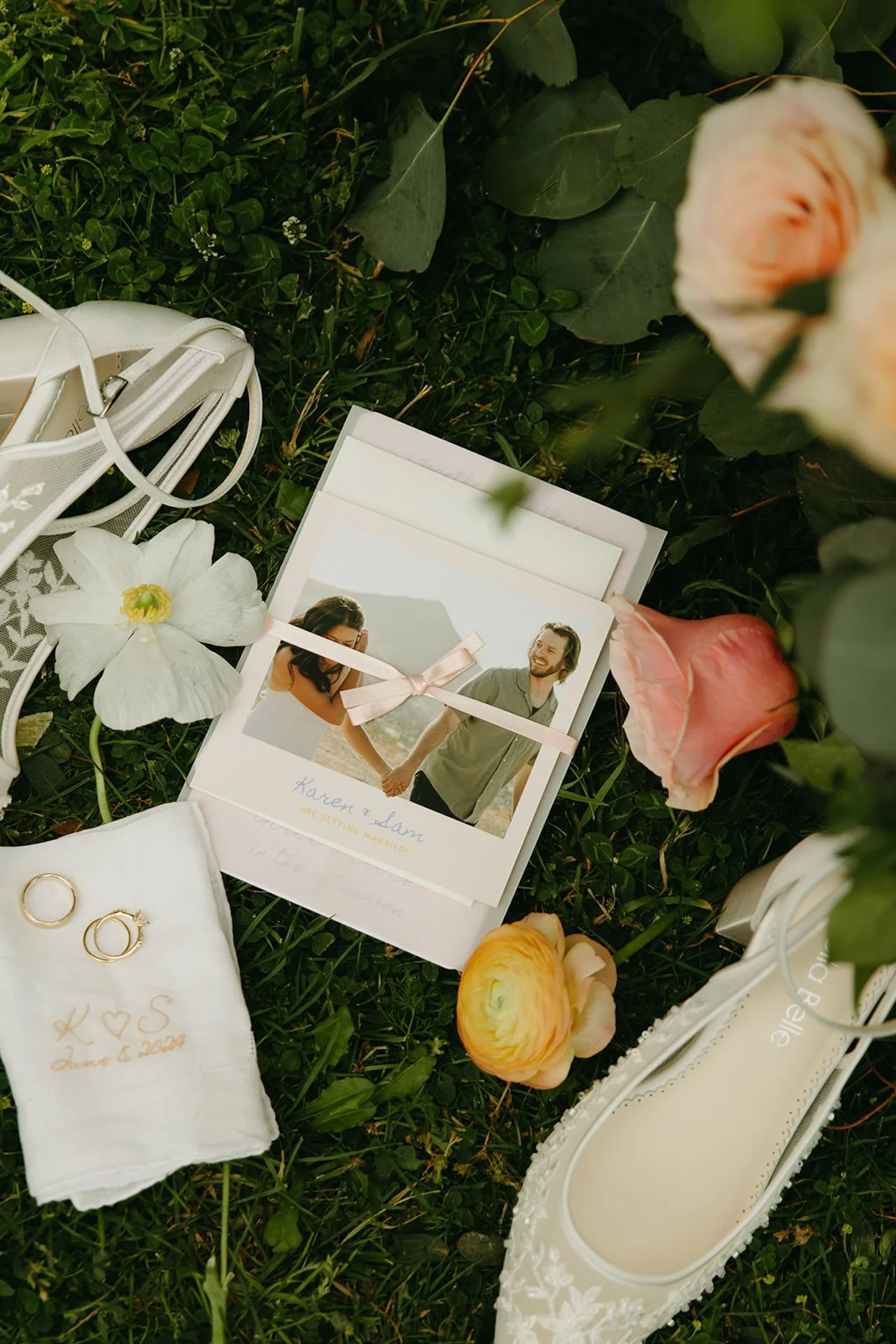 Flat lay of wedding details including rings, embroidered handkerchief, shoes, flowers, and invitation for an intimate wedding.