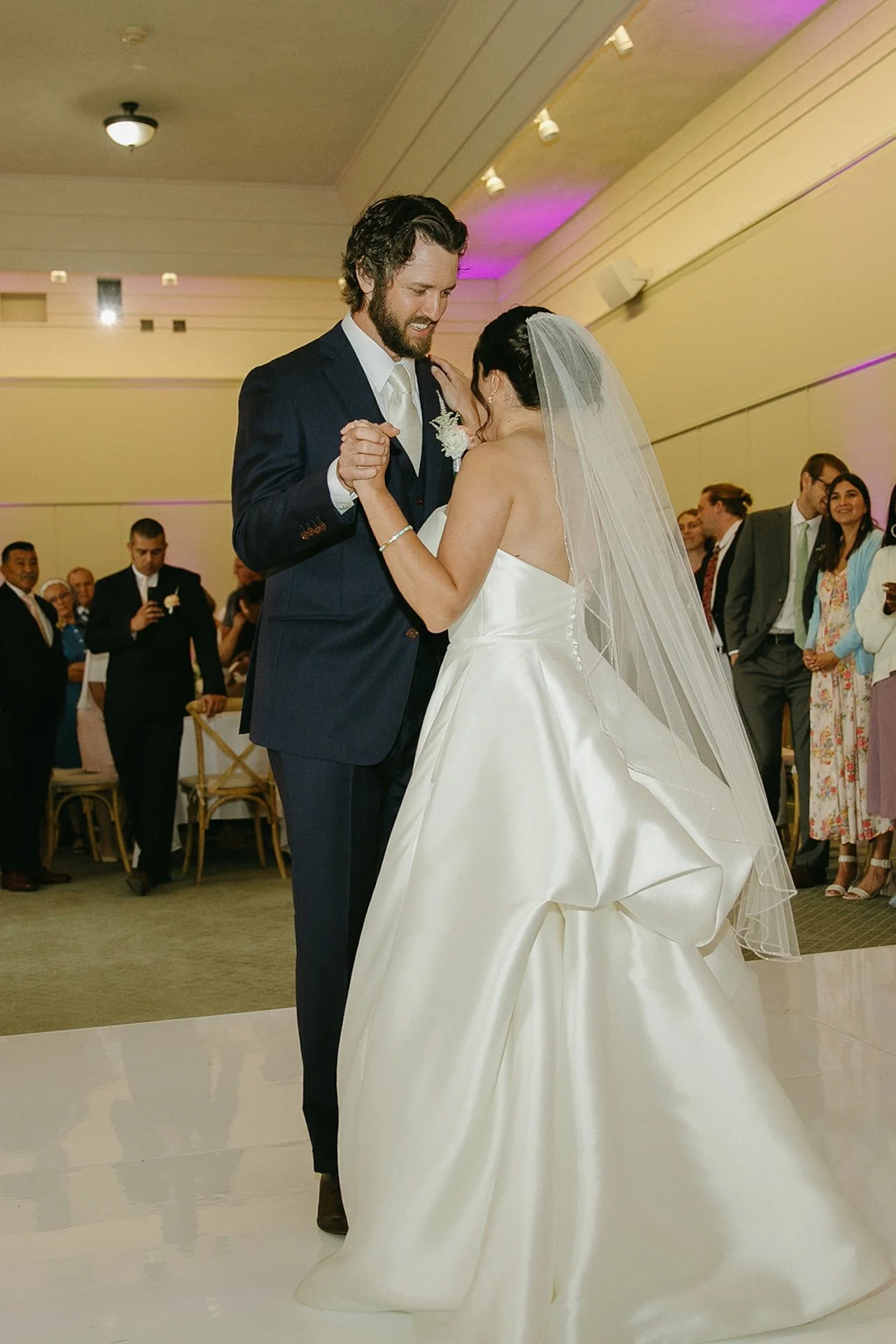 The bride and groom share their first dance, smiling warmly as they hold each other close on the dance floor during their intimate wedding.