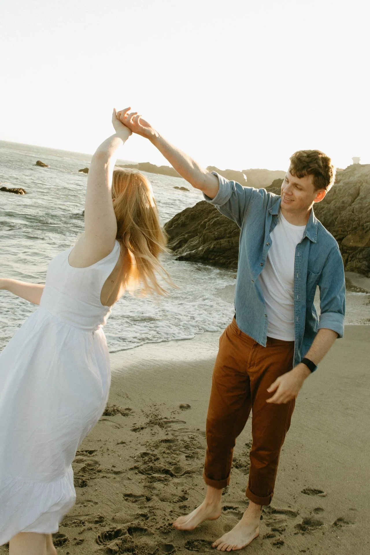 Spinning together on the sand with the ocean in the background, showing off a joyful and carefree engagement photo location.