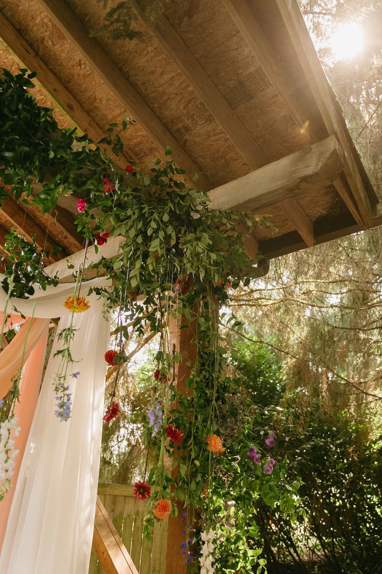 Close-up of colorful flowers and greenery hanging from the wooden beams of the ceremony arbor.