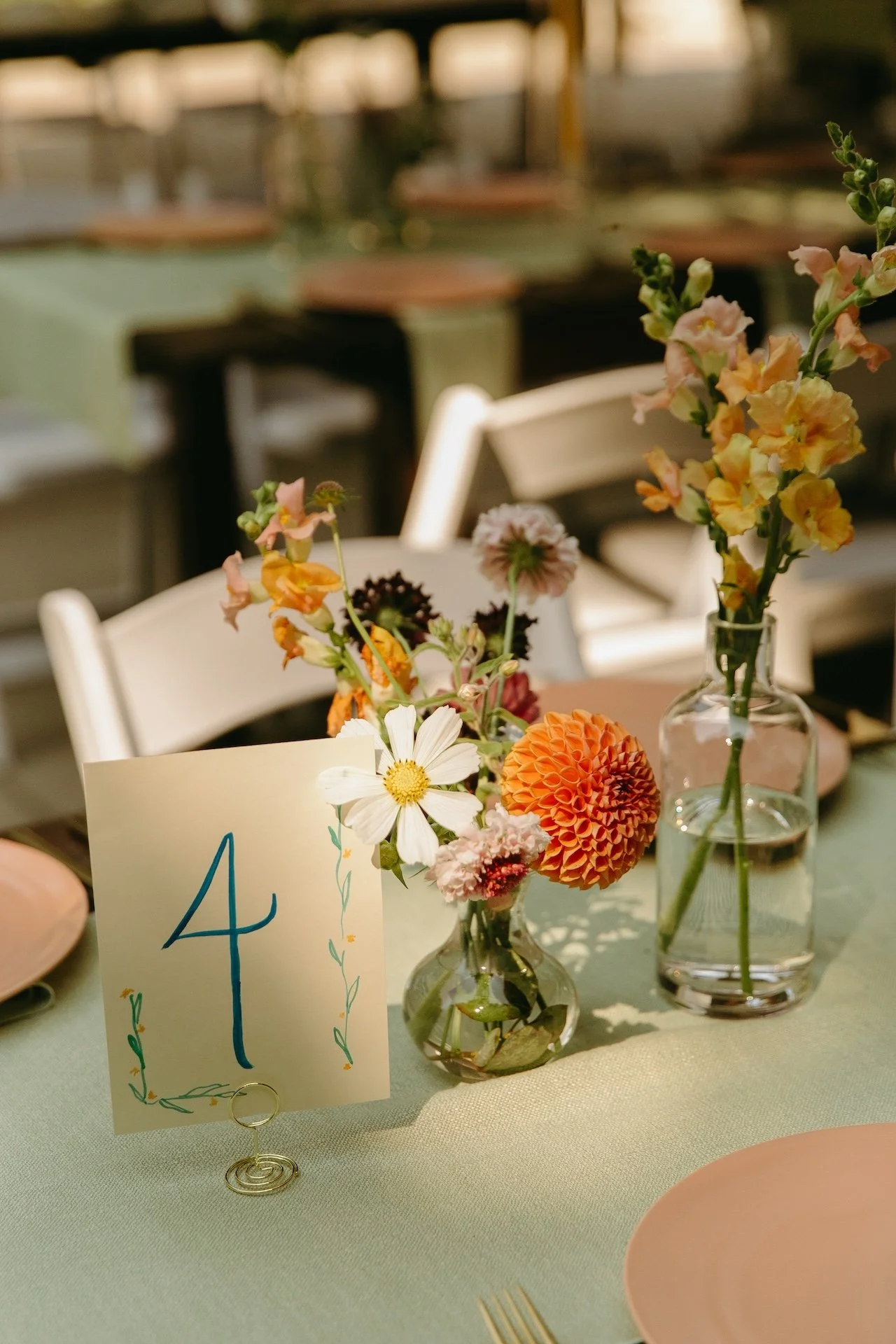 Table setting with blush plates, gold flatware, and colorful floral centerpieces marked with a handwritten table number.