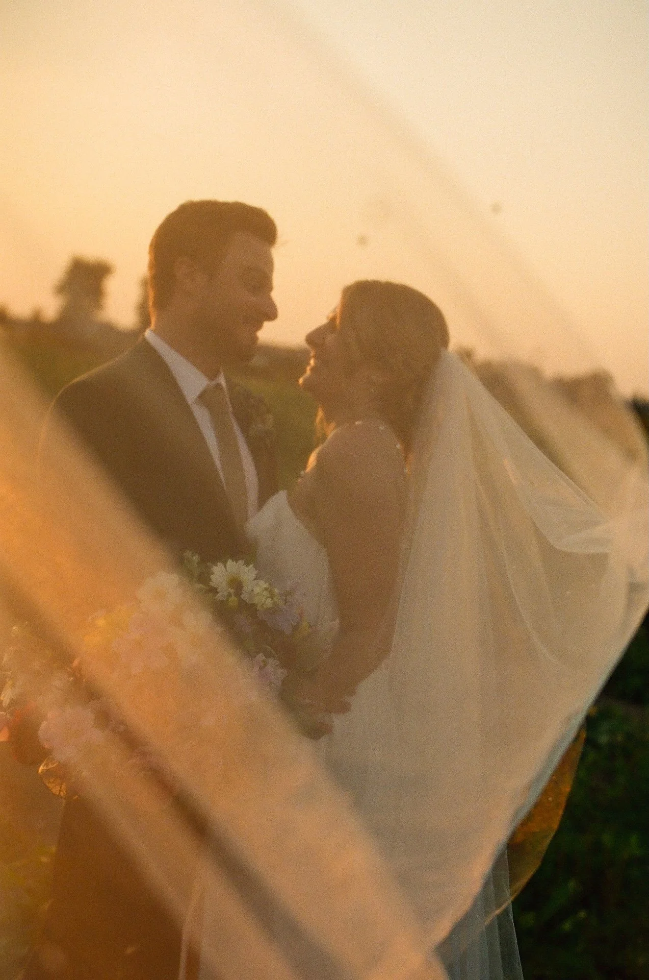 Bride smiles and leans into her groom while holding a bold bouquet of pink, peach, and white flowers at their garden party wedding.