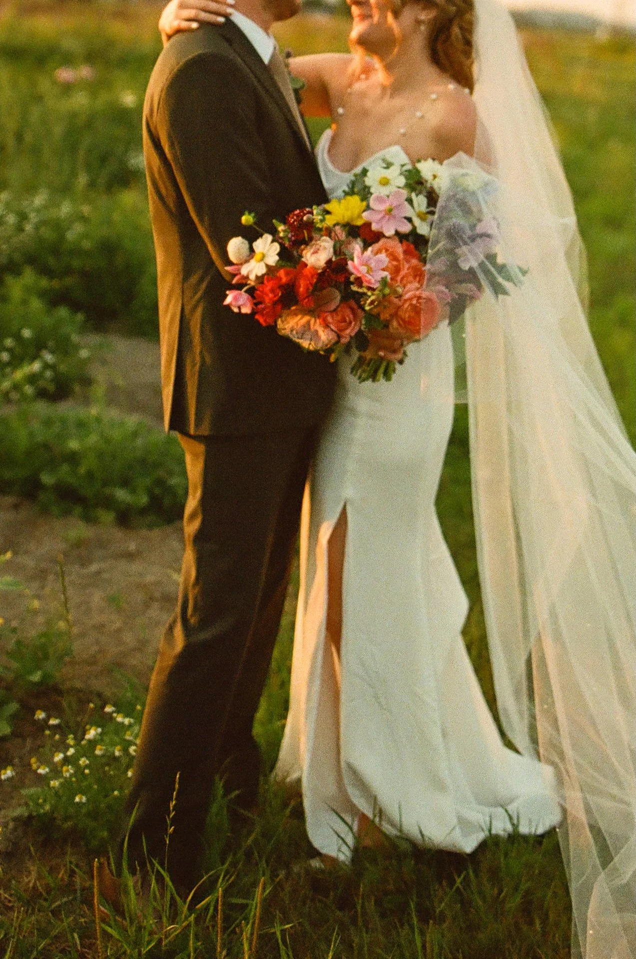 Cropped detail shot of the couple holding each other close, the bride’s bouquet full of colorful blooms resting against her gown.
