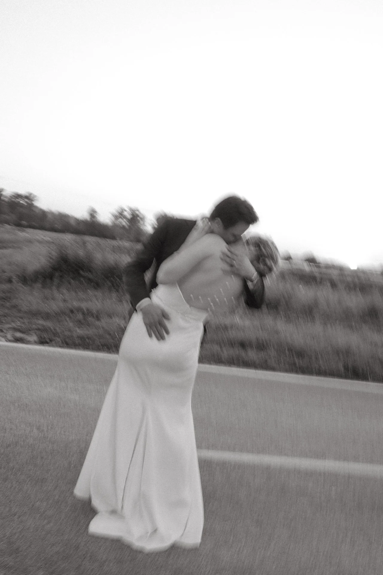 Black-and-white photo of the groom dipping the bride into a kiss in the middle of the road.