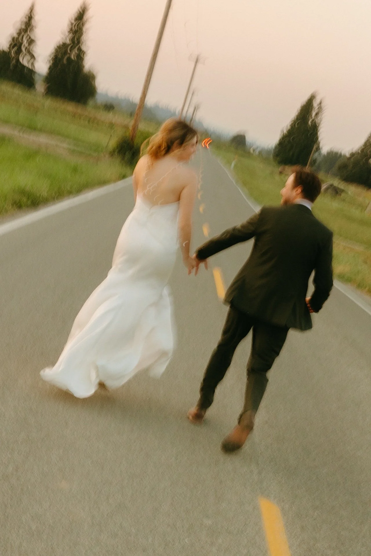 Bride and groom walk down an empty country road at dusk, holding hands after their garden party wedding.