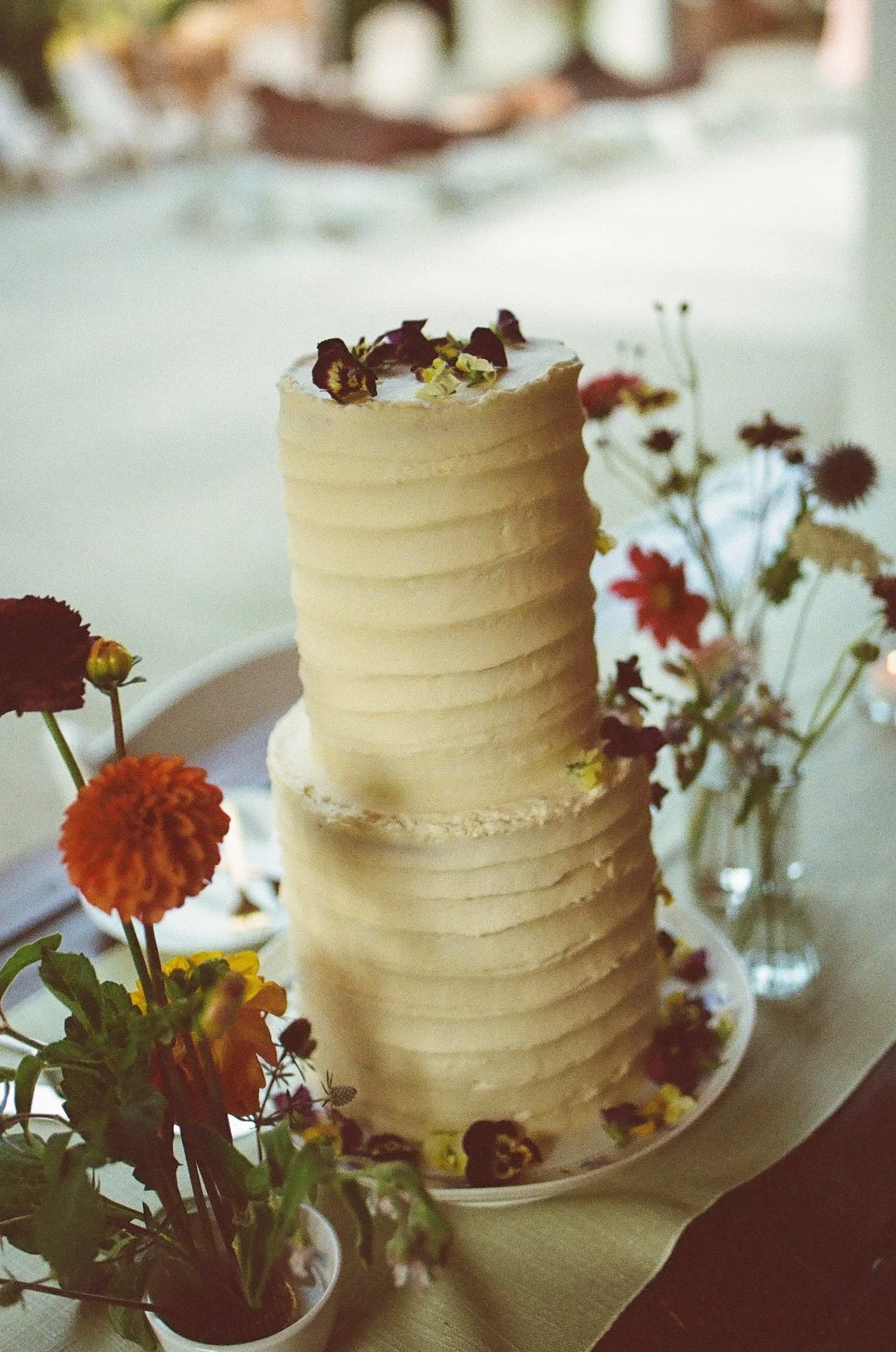 Two-tier buttercream wedding cake decorated with fresh florals and greenery.