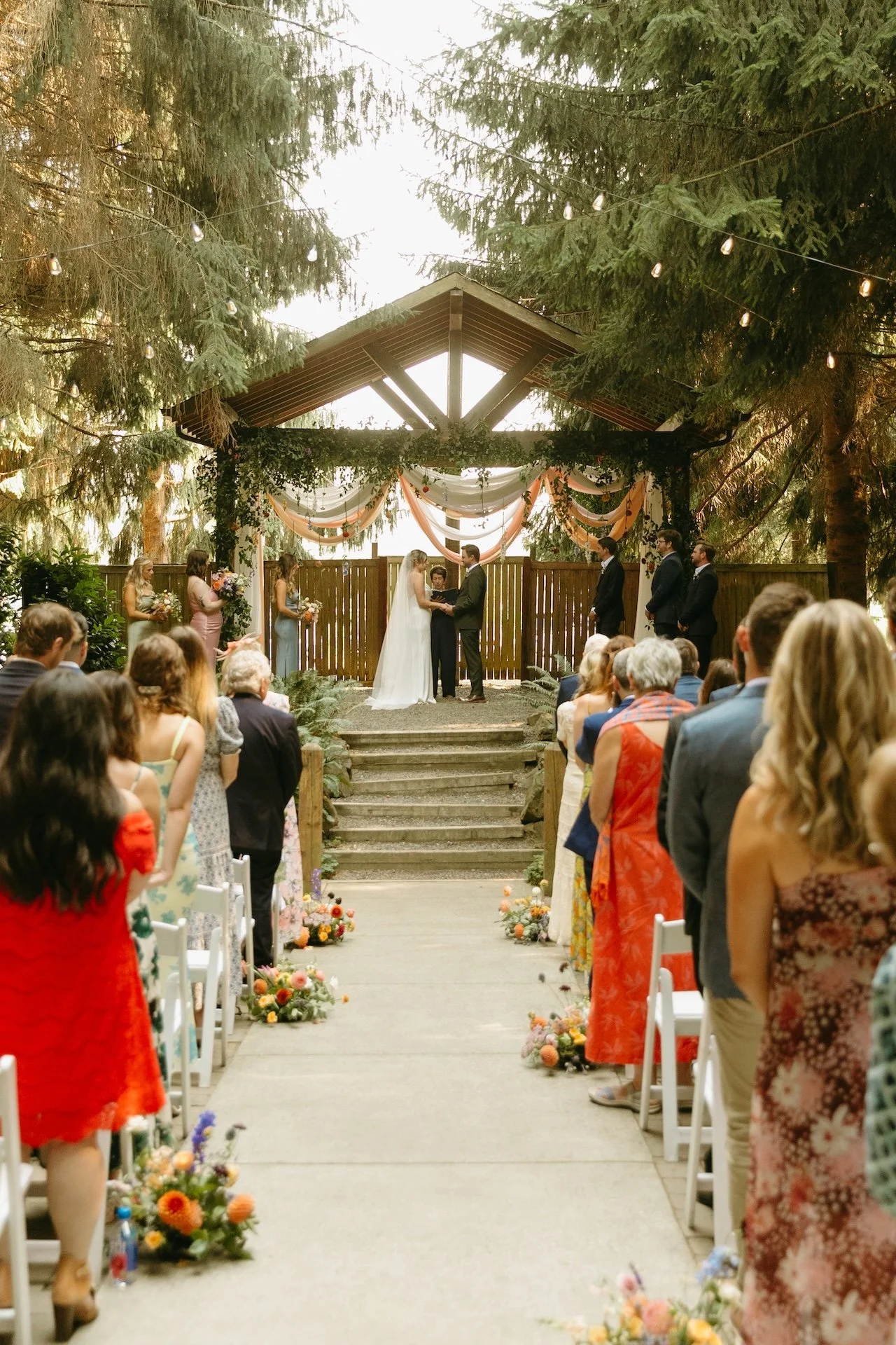 Guests stand watching the ceremony as the couple shares their vows at their garden party wedding.