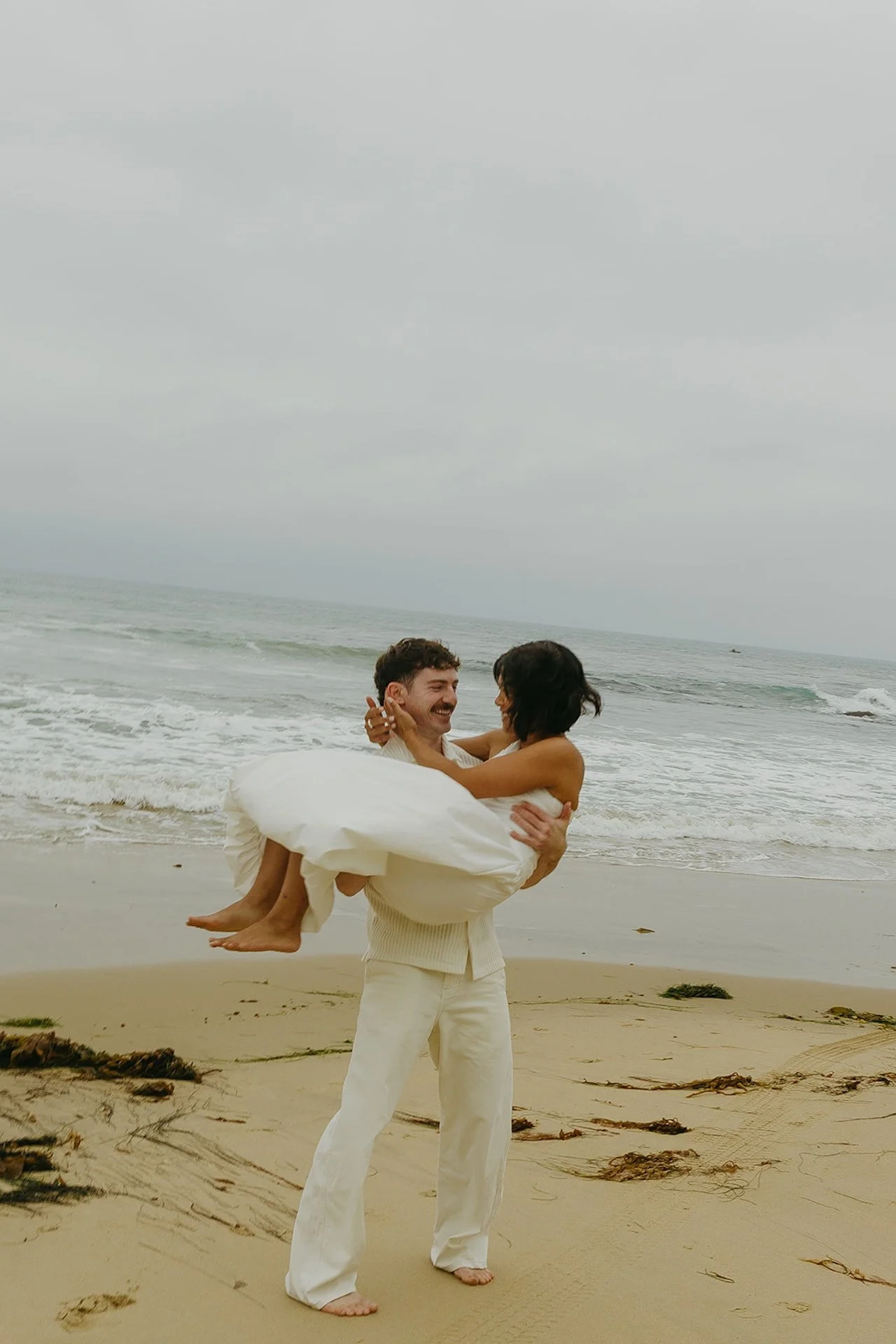 The groom carrying the bride and spinning her around on the beach during their Laguna beach elopement