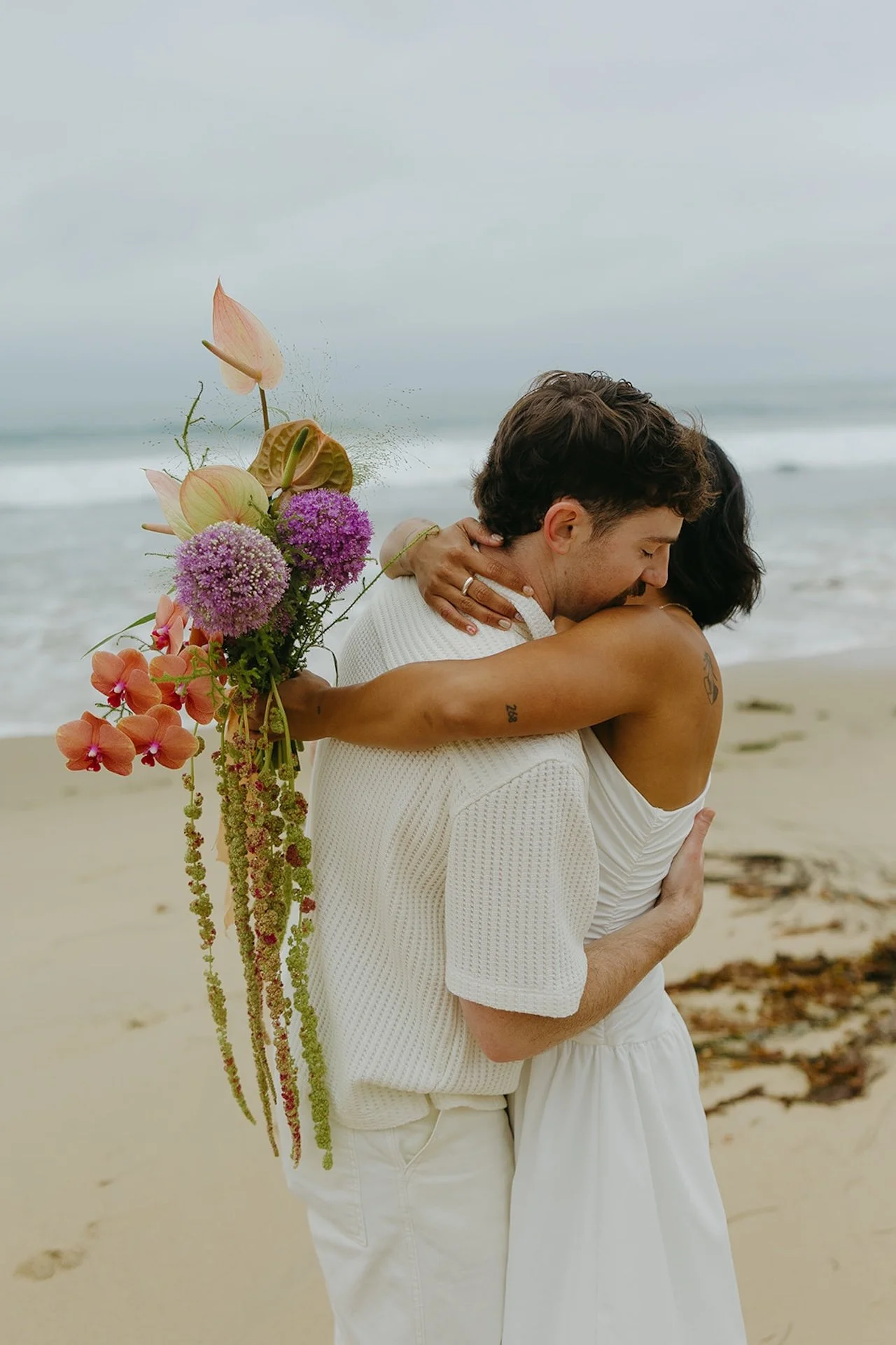 The bride and groom hugging with the waves crashing behind them during their elopement on the beach