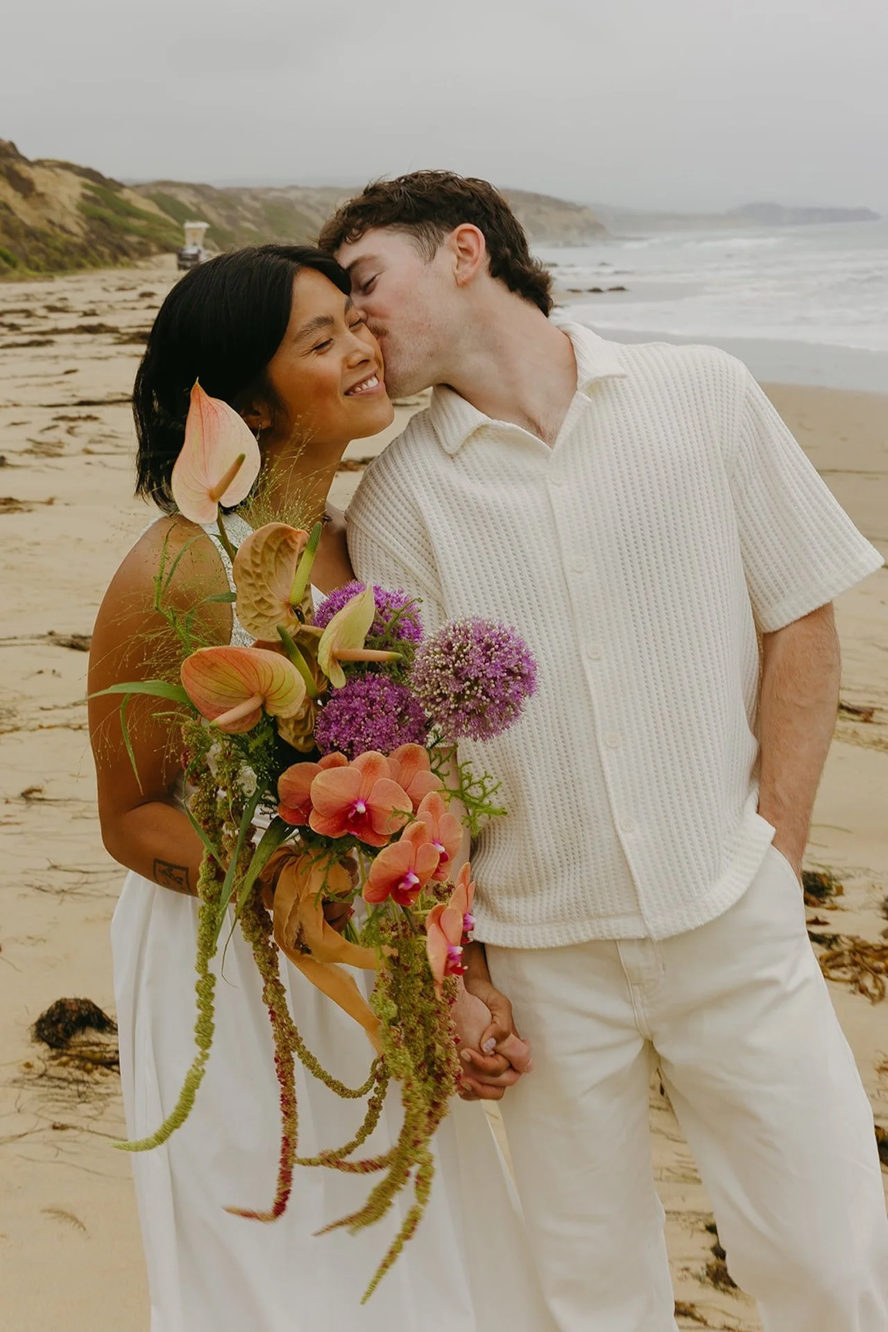 The groom kissing the brides cheek as they walk along the beach for bride and groom portraits during their elopement on the beach