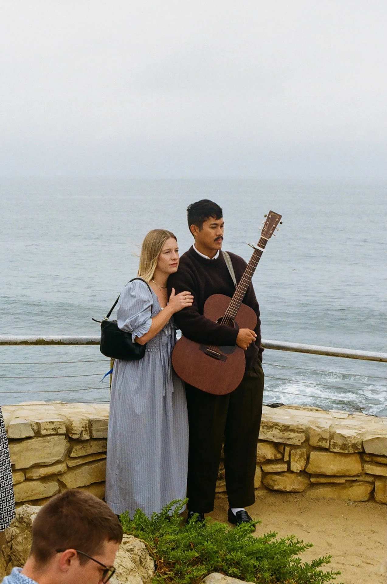 The bride and grooms friend holding a guitar to play during their elopement on the beach