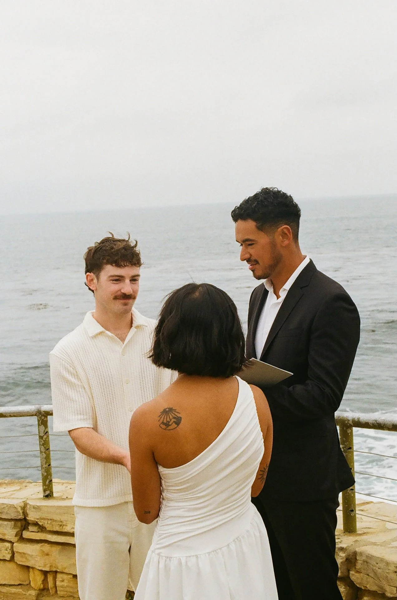 The bride and groom holding hands as they smile at each other during their beach elopement ceremony