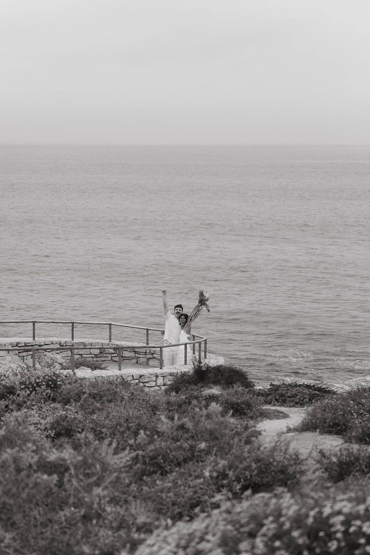 The bride and groom cheering after their wedding ceremony with the California coast in the background