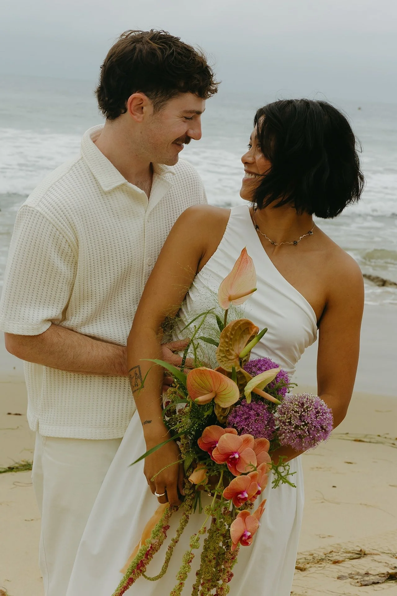 The groom hugging the bride from behind during some bride and groom portraits on the beach.
