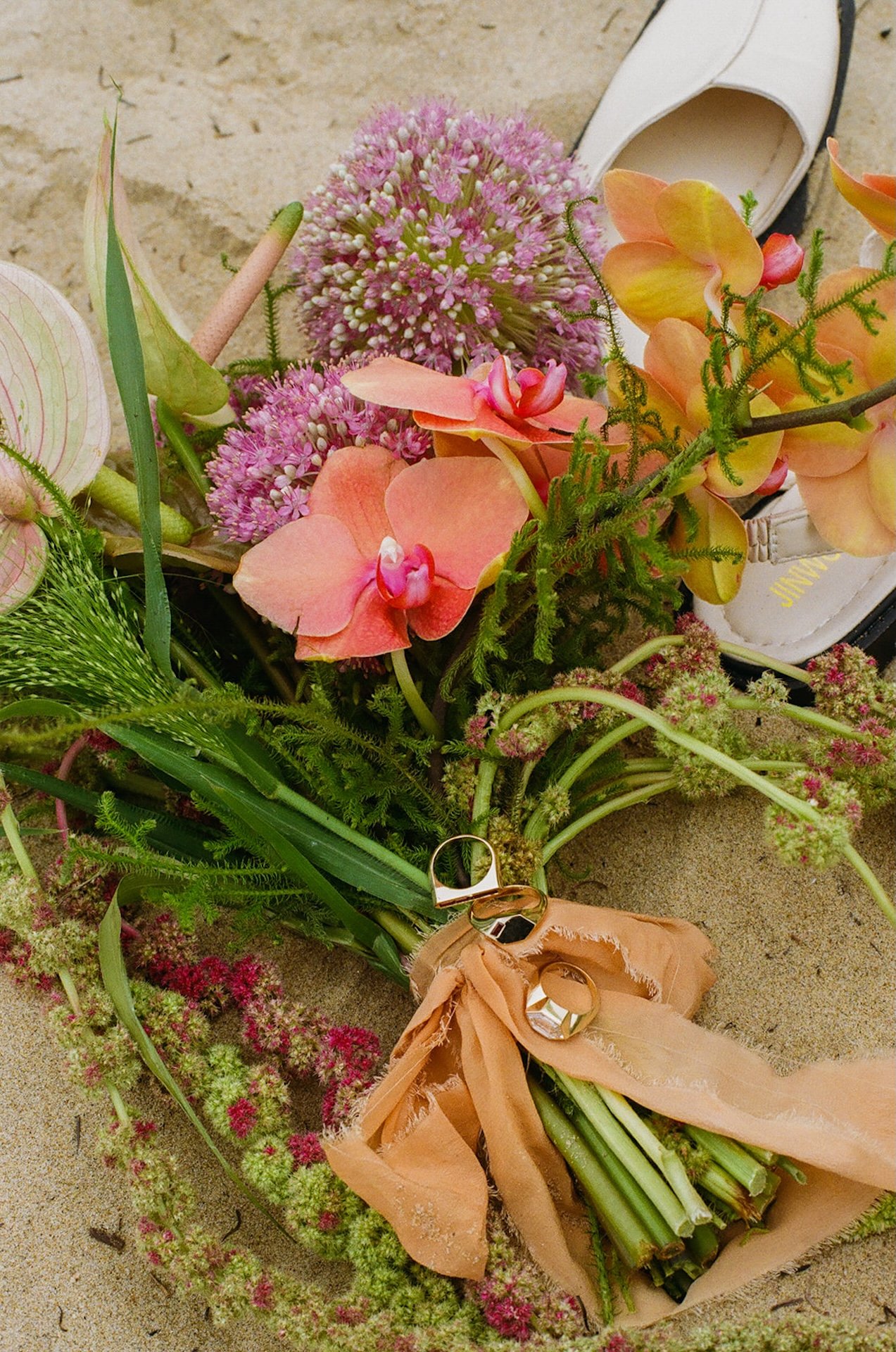 A detail flatlay of the brides bouquet and wedding shoes and the rings on a rock