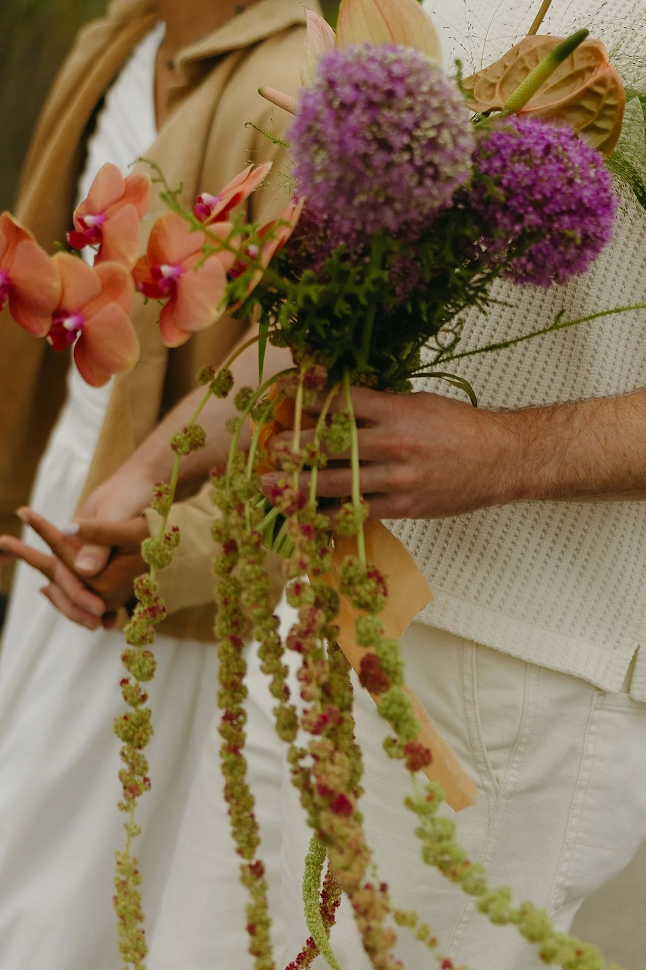 A detail shot of the bride and groom holds hands and walking to their elopement on the beach