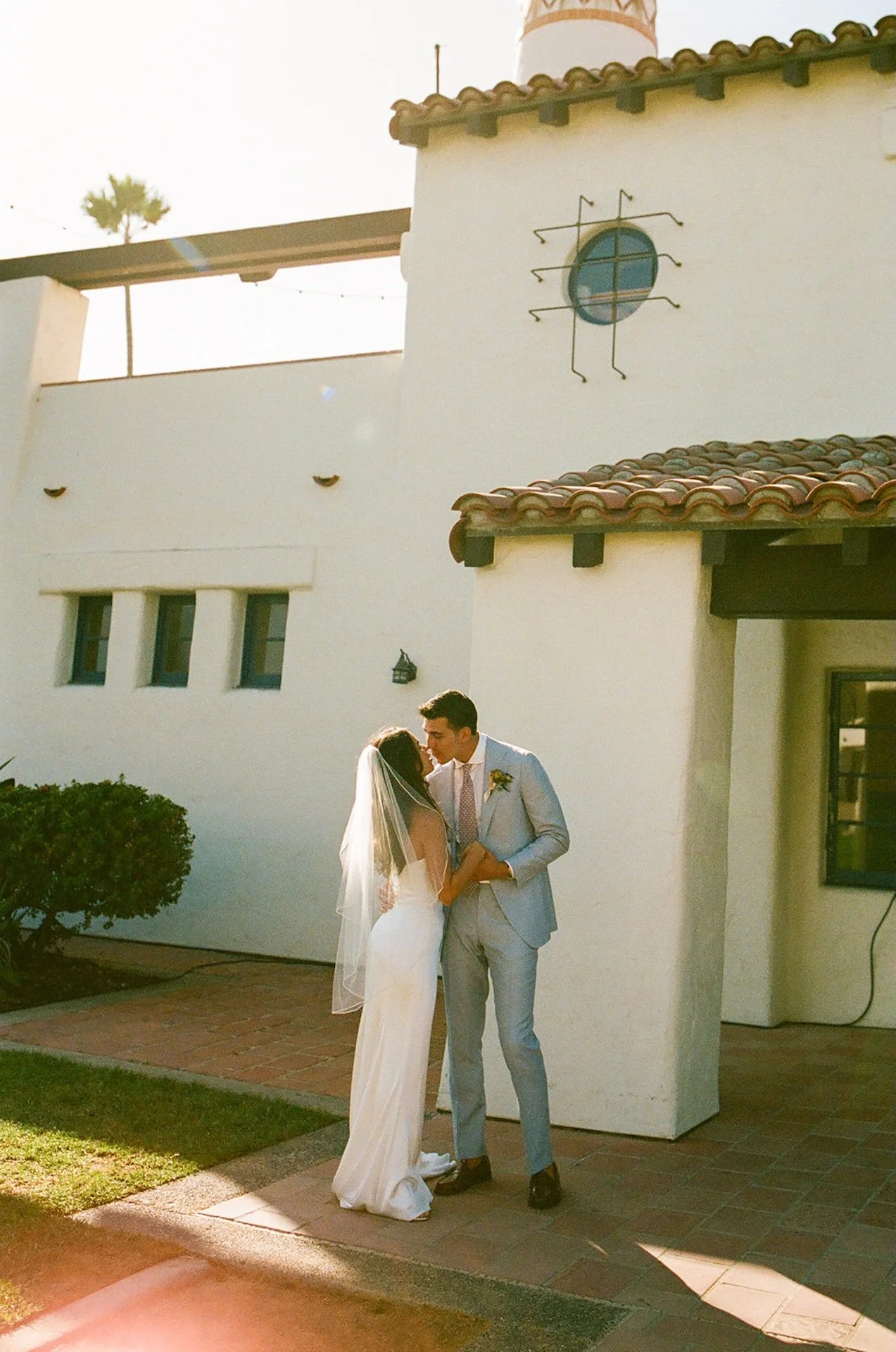 The couple shares a quiet kiss in the sunshine against the venue’s creamy stucco walls.