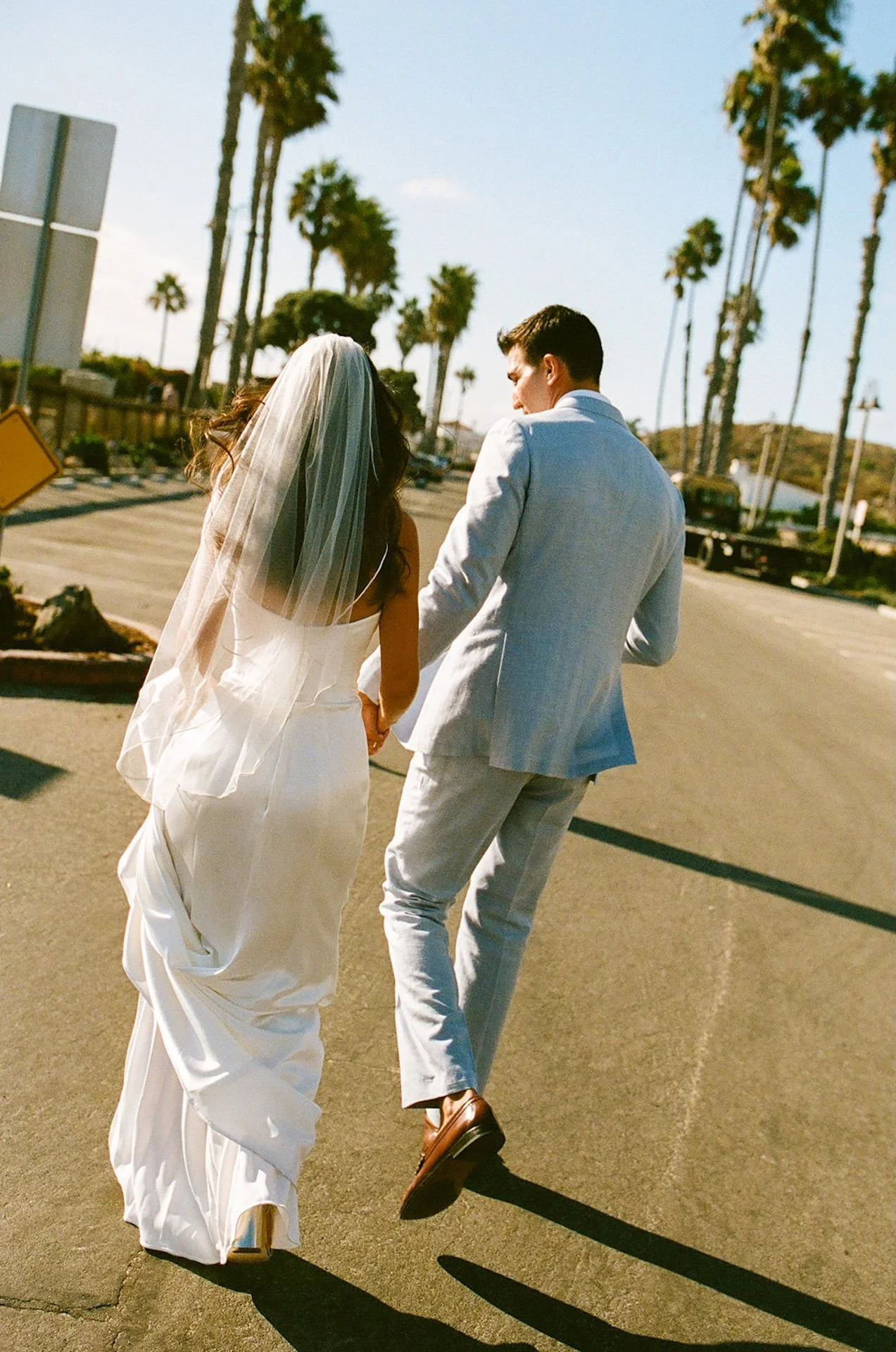 The newlyweds run together down the road, her veil flowing behind her at a San Juan Capistrano Wedding Venue.