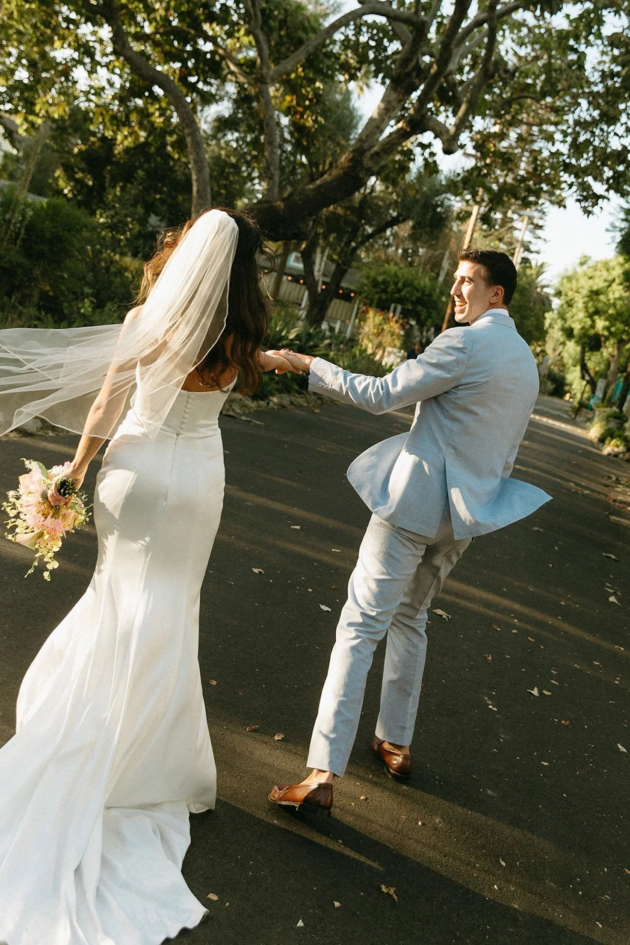 The couple laughs while walking through a tree-lined path at a San Juan Capistrano Wedding Venue.
