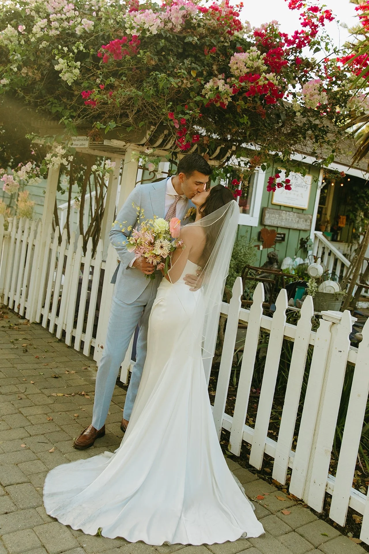 The bride and groom share a kiss beneath blooming bougainvillea at a San Juan Capistrano Wedding Venue.