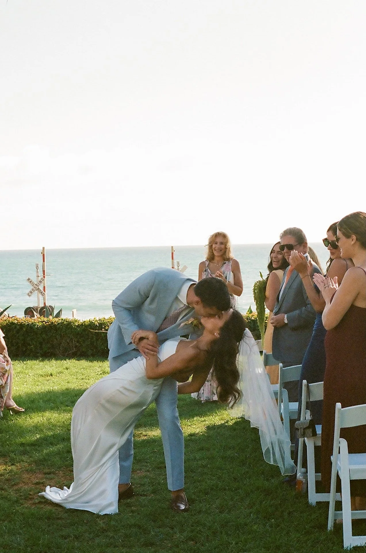 The newlyweds share a joyful dip-kiss surrounded by cheering guests at a San Juan Capistrano Wedding Venue.