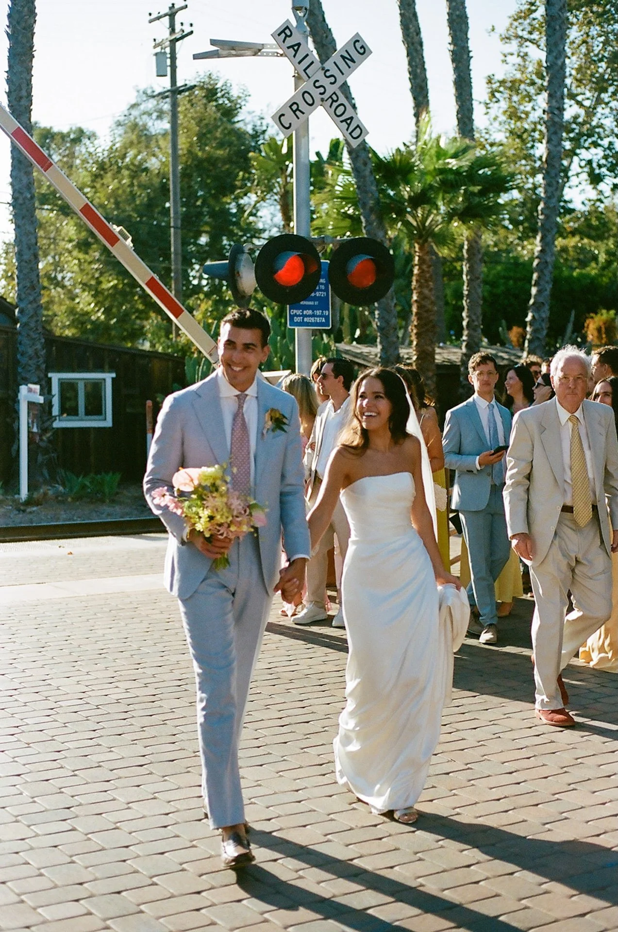The bride and groom walk hand in hand past a railroad crossing sign at a San Juan Capistrano Wedding Venue.