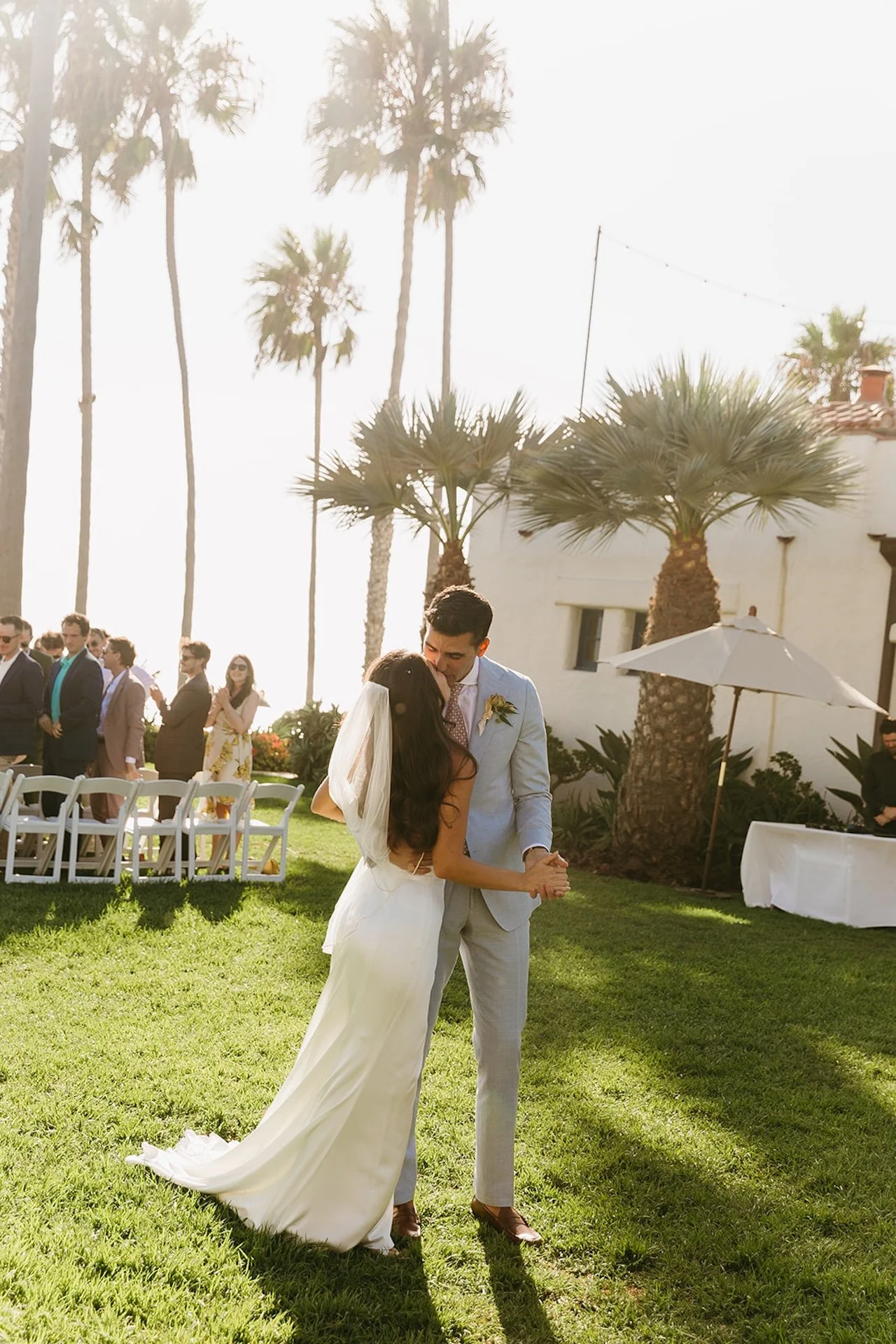 The couple shares a soft first dance on the grass surrounded by palms at a San Juan Capistrano Wedding Venue.
