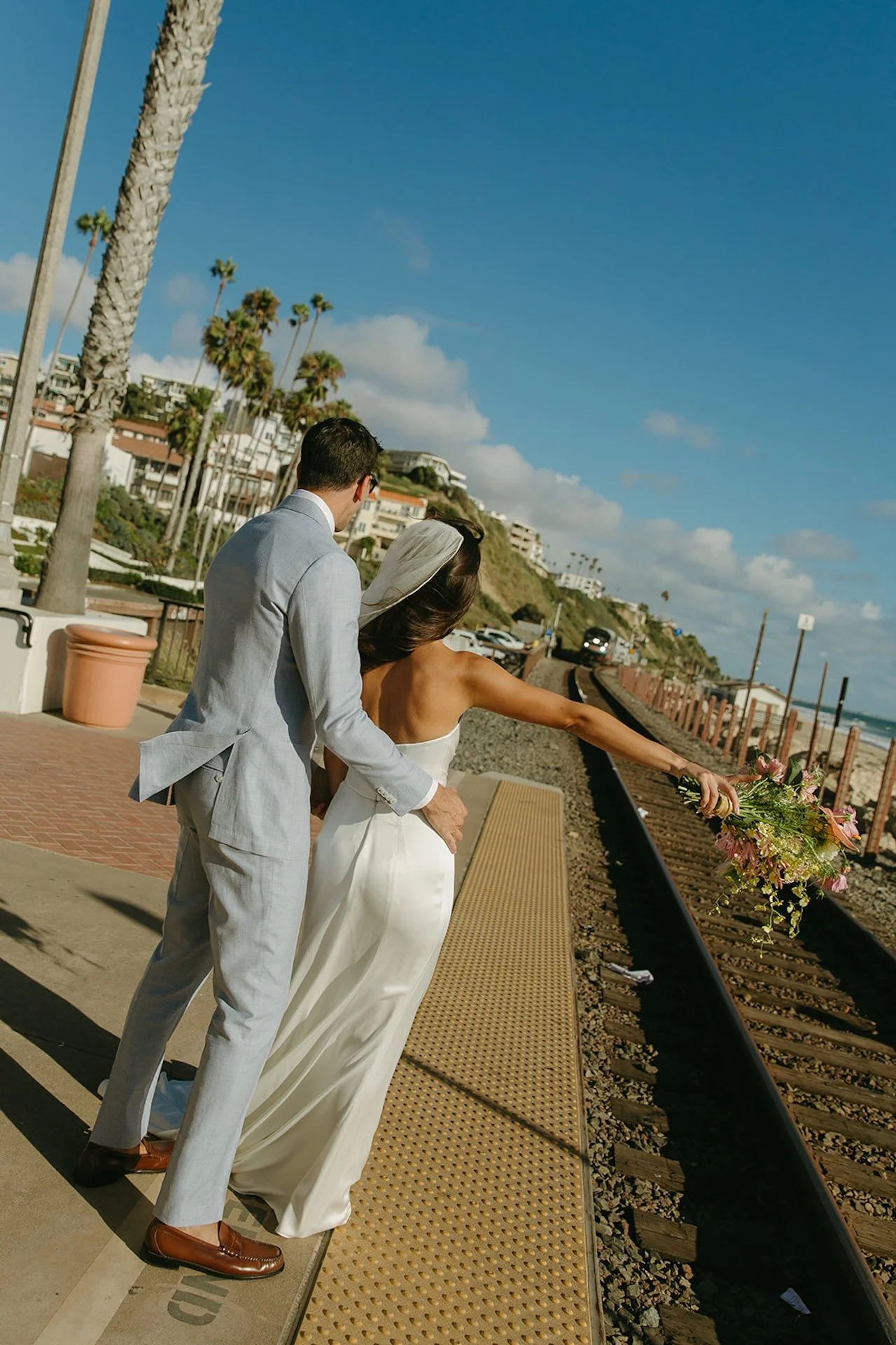 The couple stands on the train platform with ocean views at a San Juan Capistrano Wedding Venue.