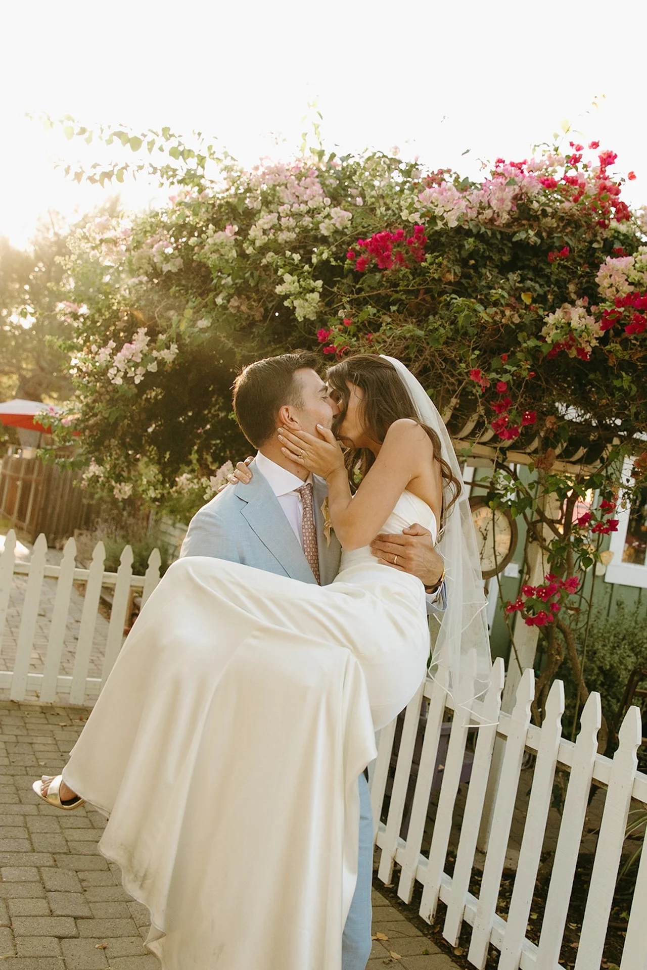 The groom carrying the bride during their bride and groom portraits outside of their San Juan Capistrano Wedding Venue