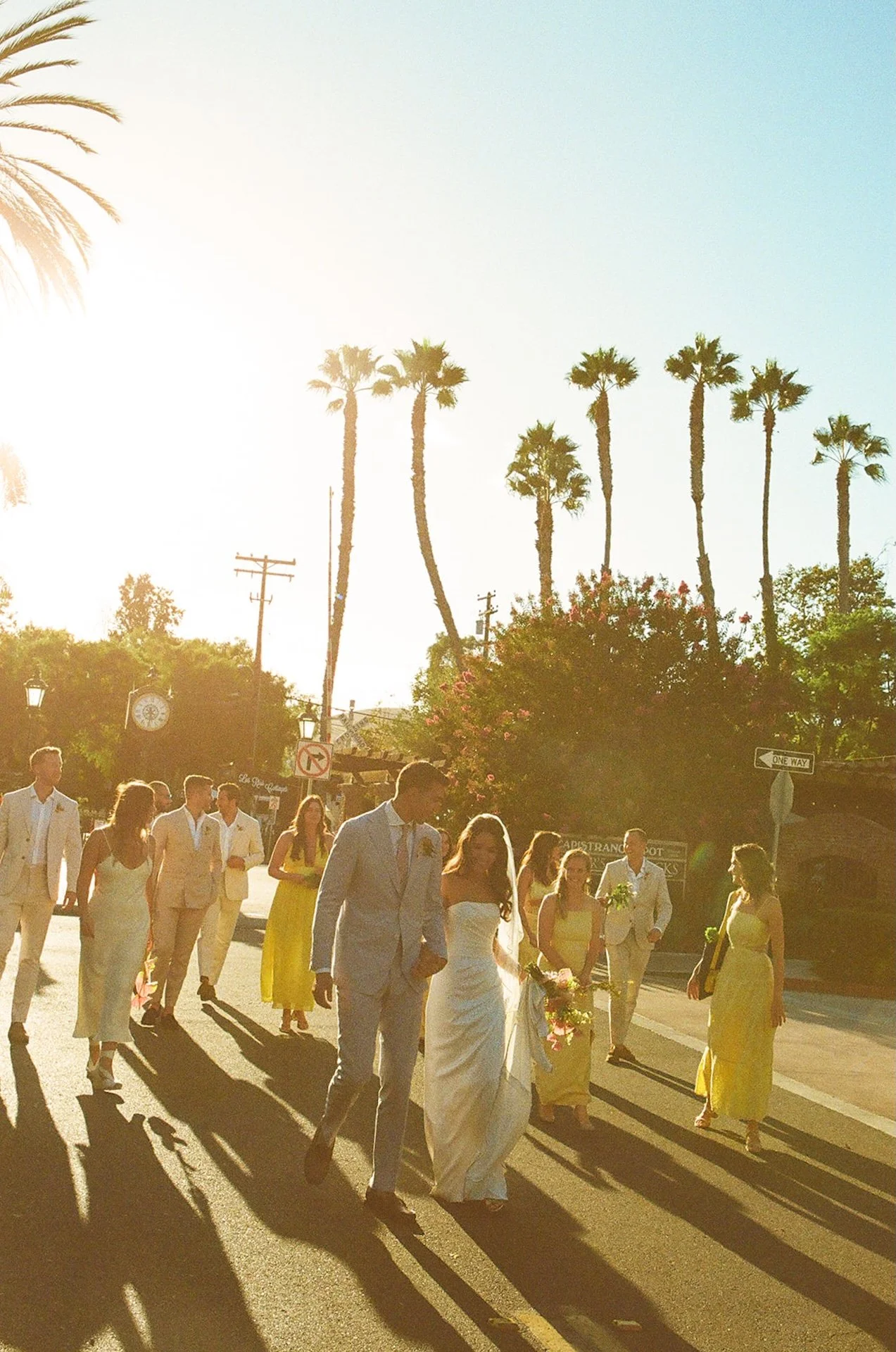 The bride and groom walking hand in hand across the street with their wedding party on their way to their San Juan Capistrano Wedding Venue