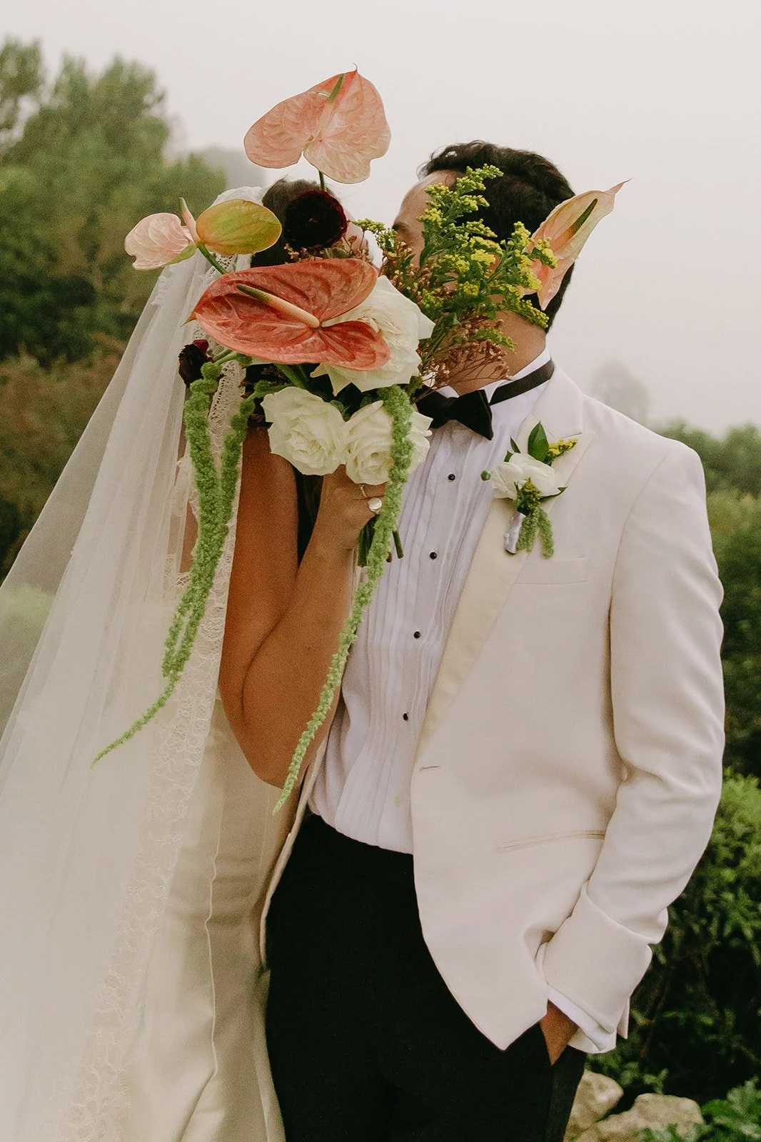 Close-up of the couple playfully hiding their kiss behind the bouquet during their La Venta Inn wedding.