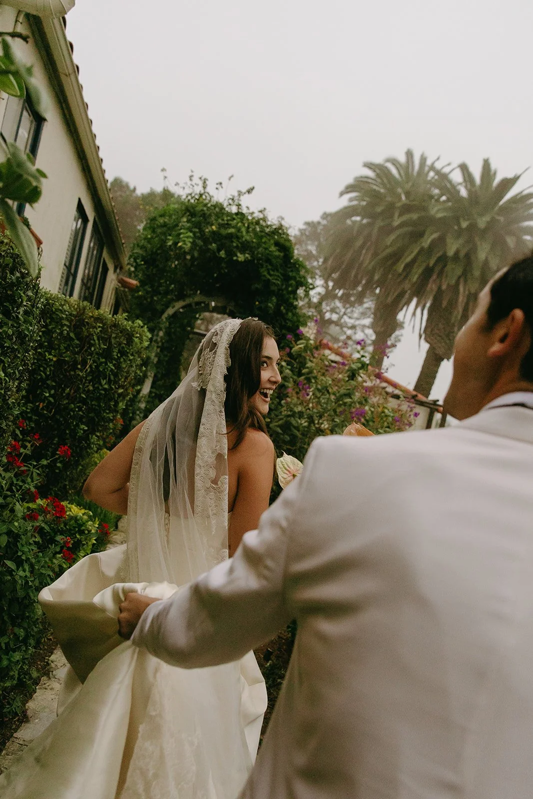Bride laughing over her shoulder as the groom follows her through the garden paths, photographed by a Los Angeles wedding photographer.