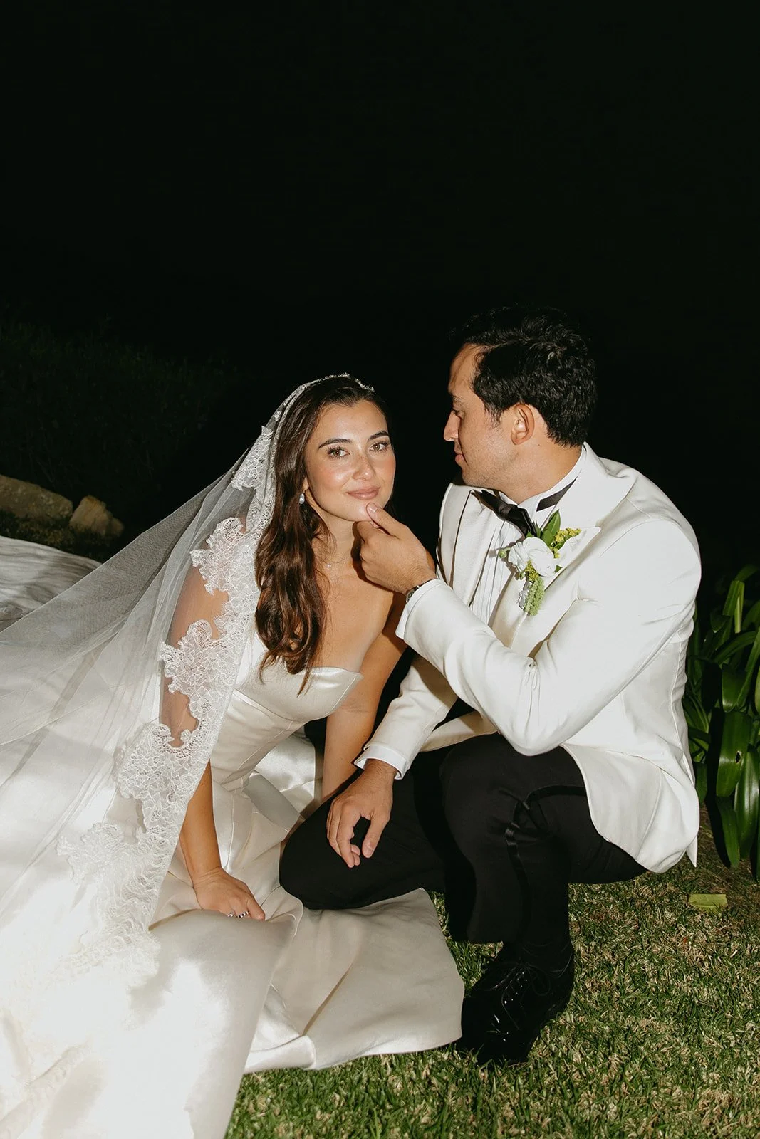 The couple sitting together on the grass as the groom gently lifts the bride’s chin, captured in a candid moment by a Los Angeles wedding photographer.