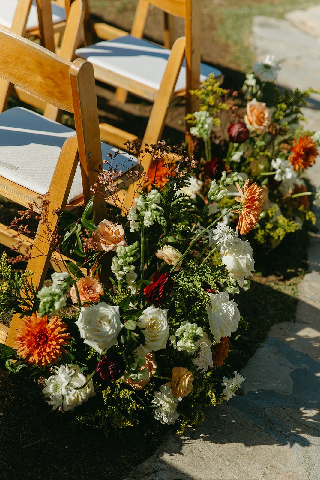 Close-up of ceremony flowers arranged beside wooden chairs, photographed by a Los Angeles wedding photographer.