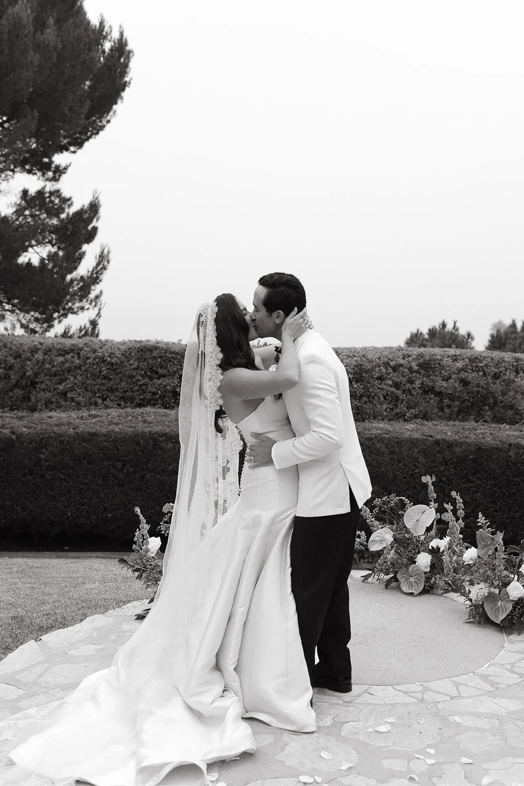 Wide ceremony shot showing guests gathered around the couple on a stone terrace overlooking the ocean.
