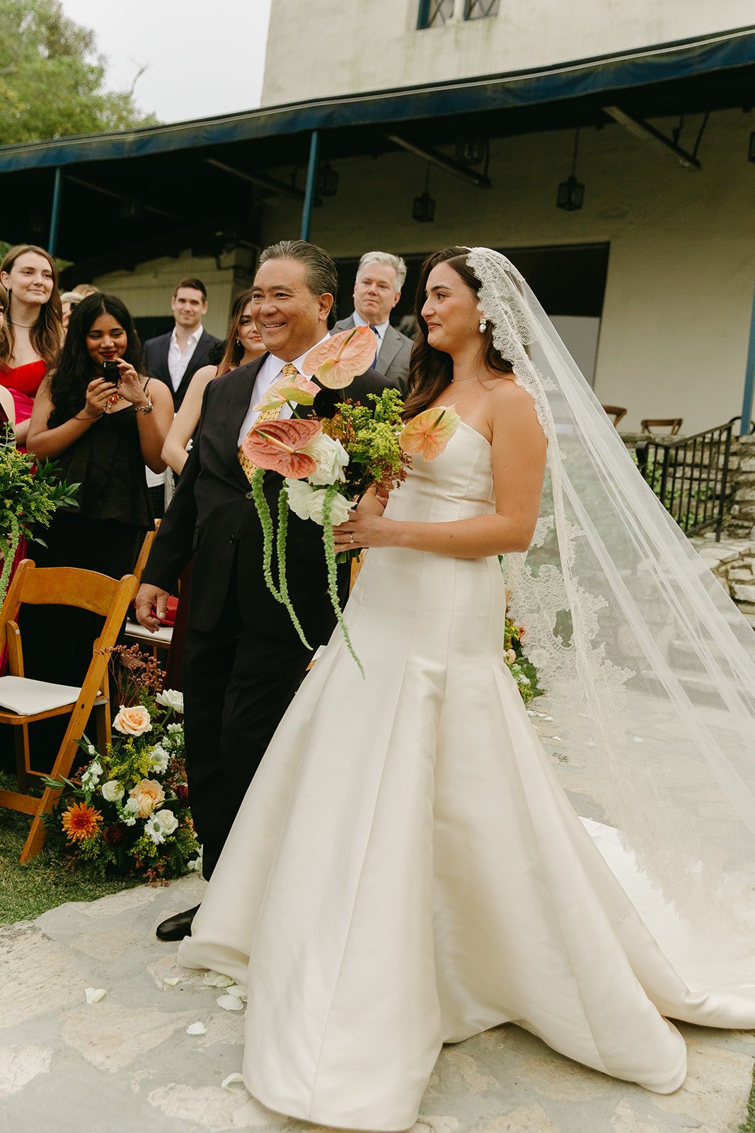 Bride walking down the aisle with her father as guests look on.