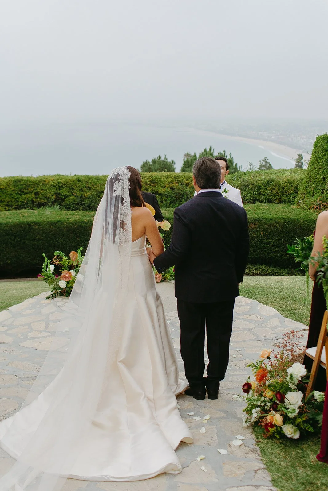 Full view of the bride’s structured gown and lace veil flowing behind her.