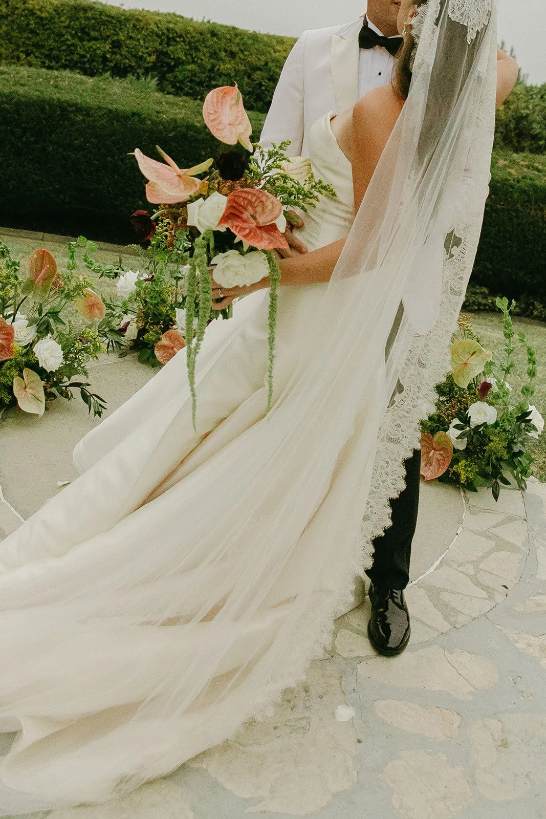 Close-up of the bride’s gown and bouquet as she stands beside the groom during portraits.