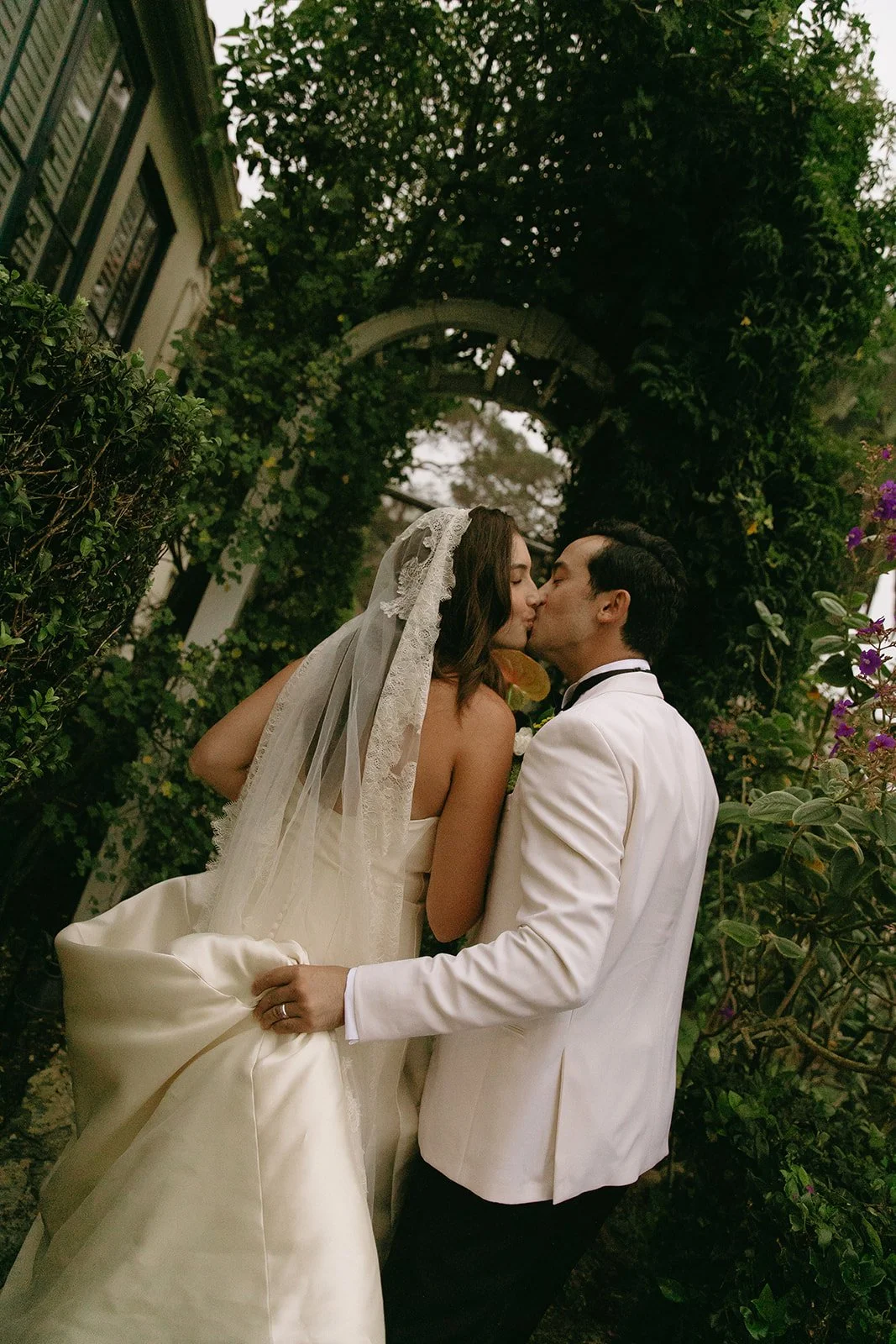 Bride and groom sharing a quiet kiss beneath garden greenery at a Historic Wedding Venue.