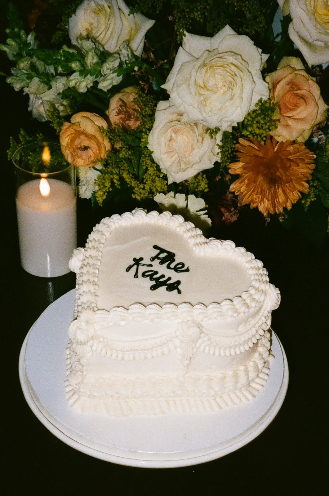 Heart-shaped wedding cake displayed on a table beside candlelight and floral arrangements.