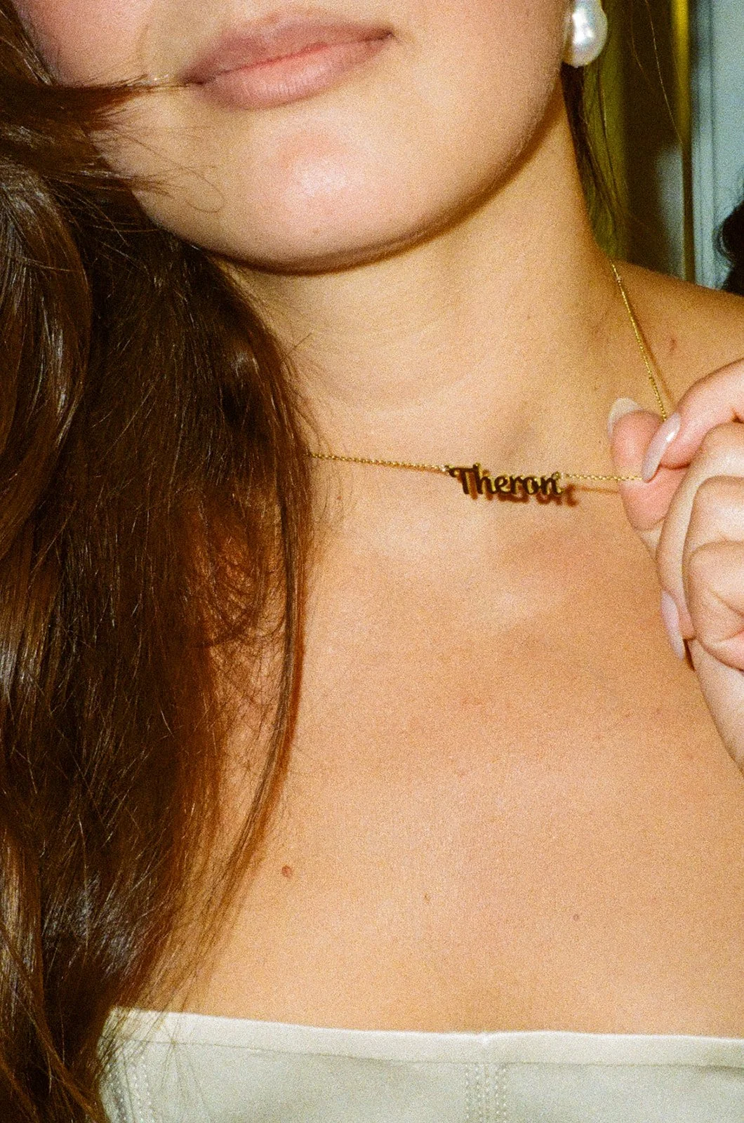 Close-up of the bride’s pearl earrings and name necklace resting against her collarbone.