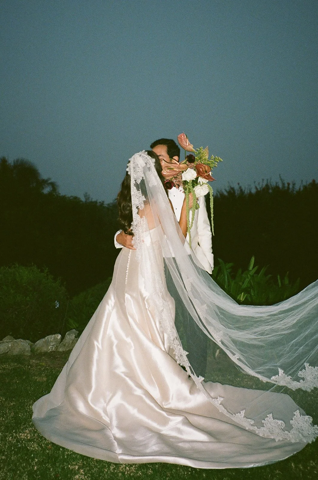 Bride and groom sharing a quiet kiss at night as her veil flows behind them at a Historic Wedding Venue.