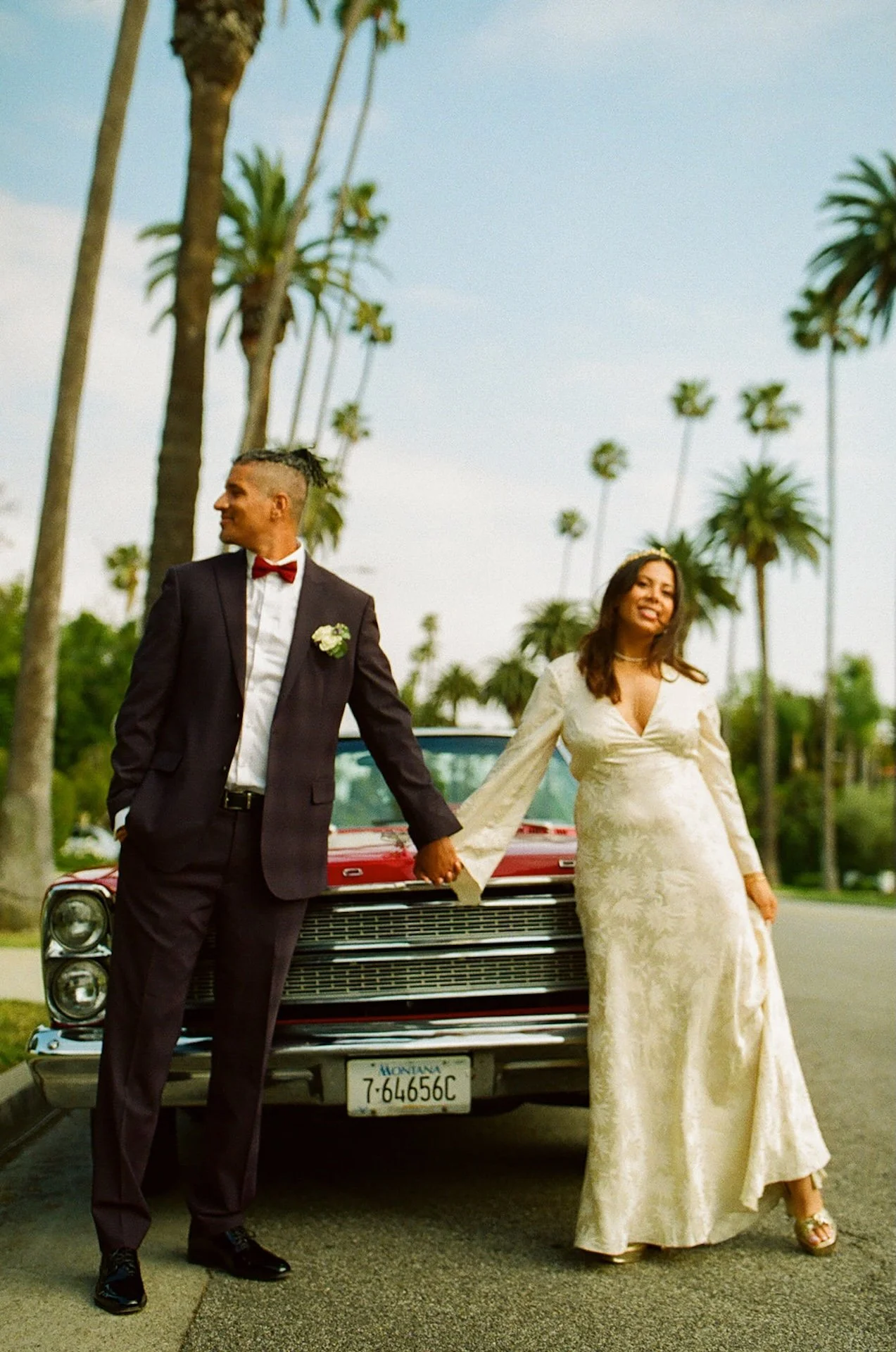 Newled holding hands and standing in front of a red convertable