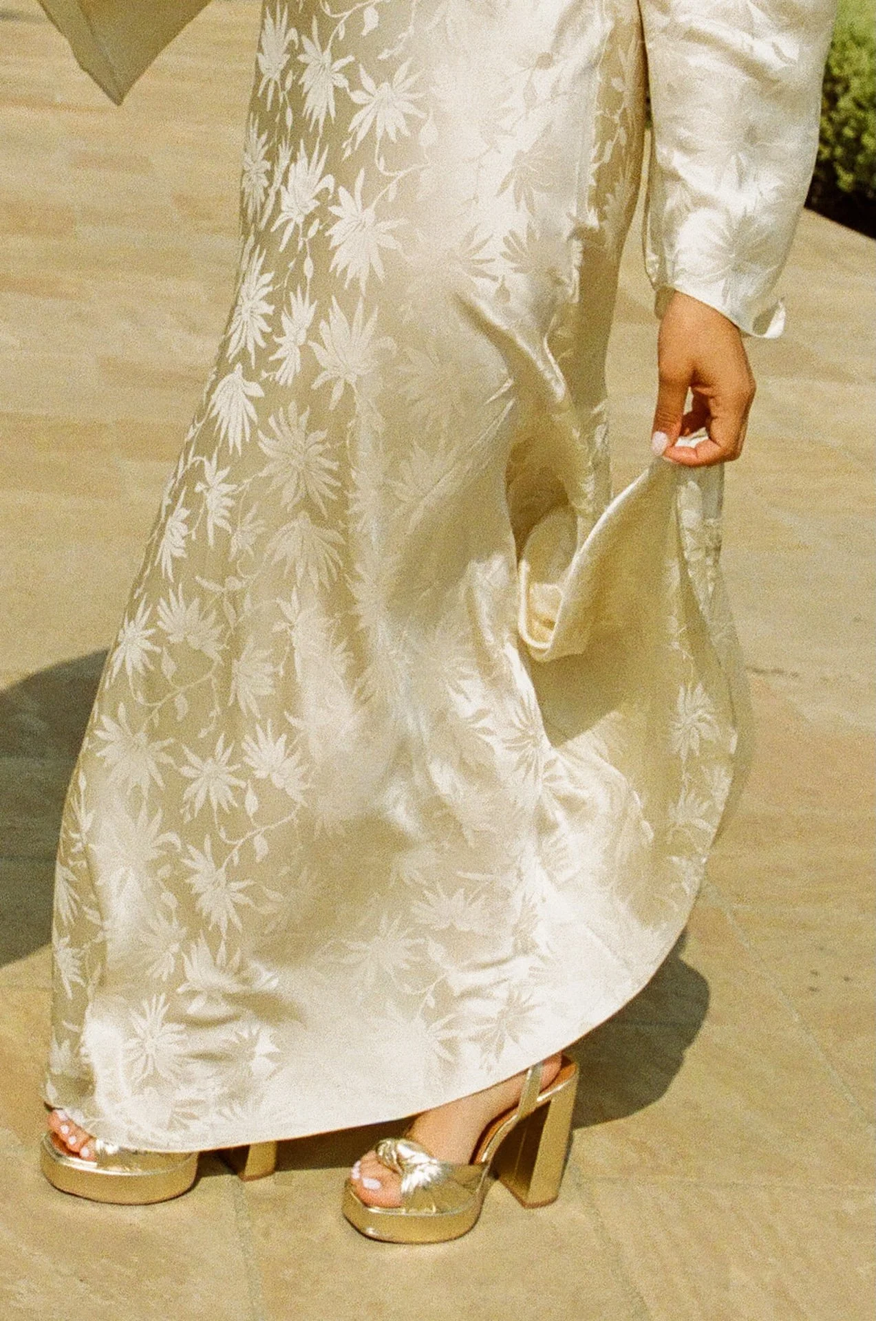 Detail photo of the bride grasping her silky floral elopement dress with the sun shining on it.